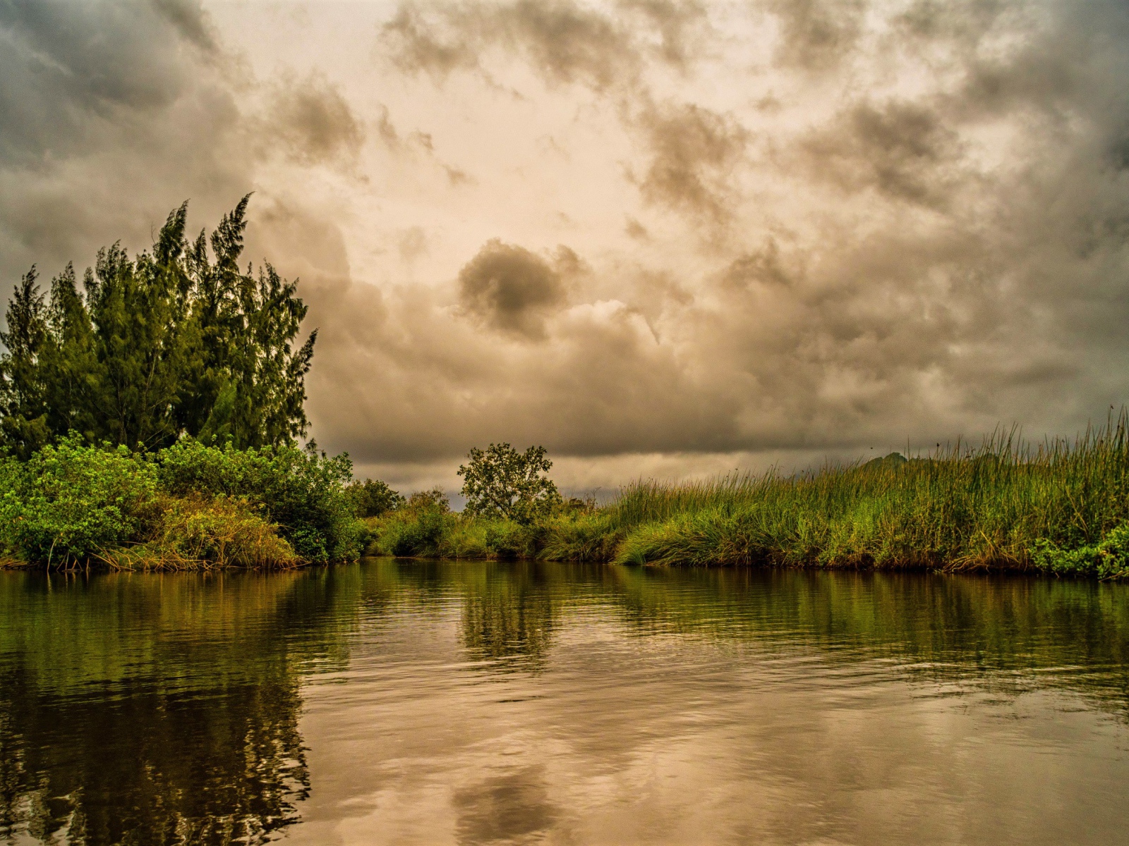 Облака над озером с покрыми зеленой травой берегами