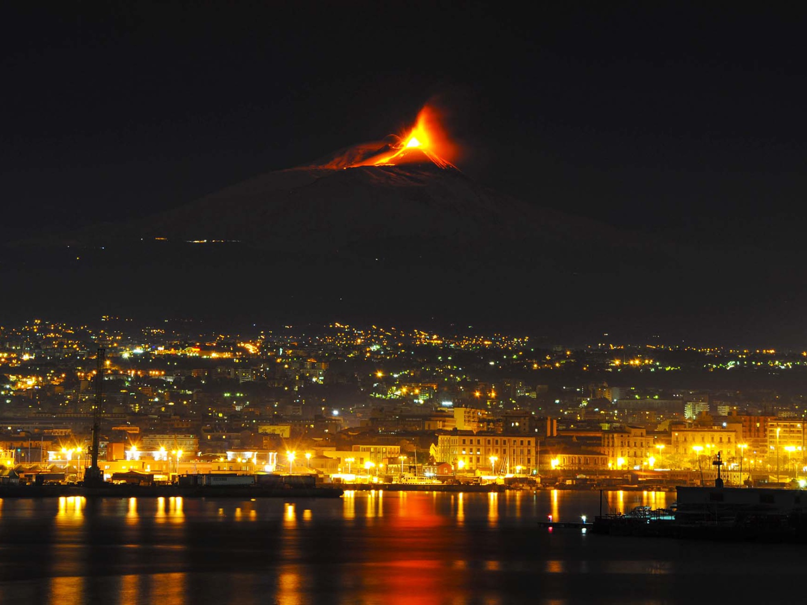 Awakening of the volcano Etna in the background of the night city