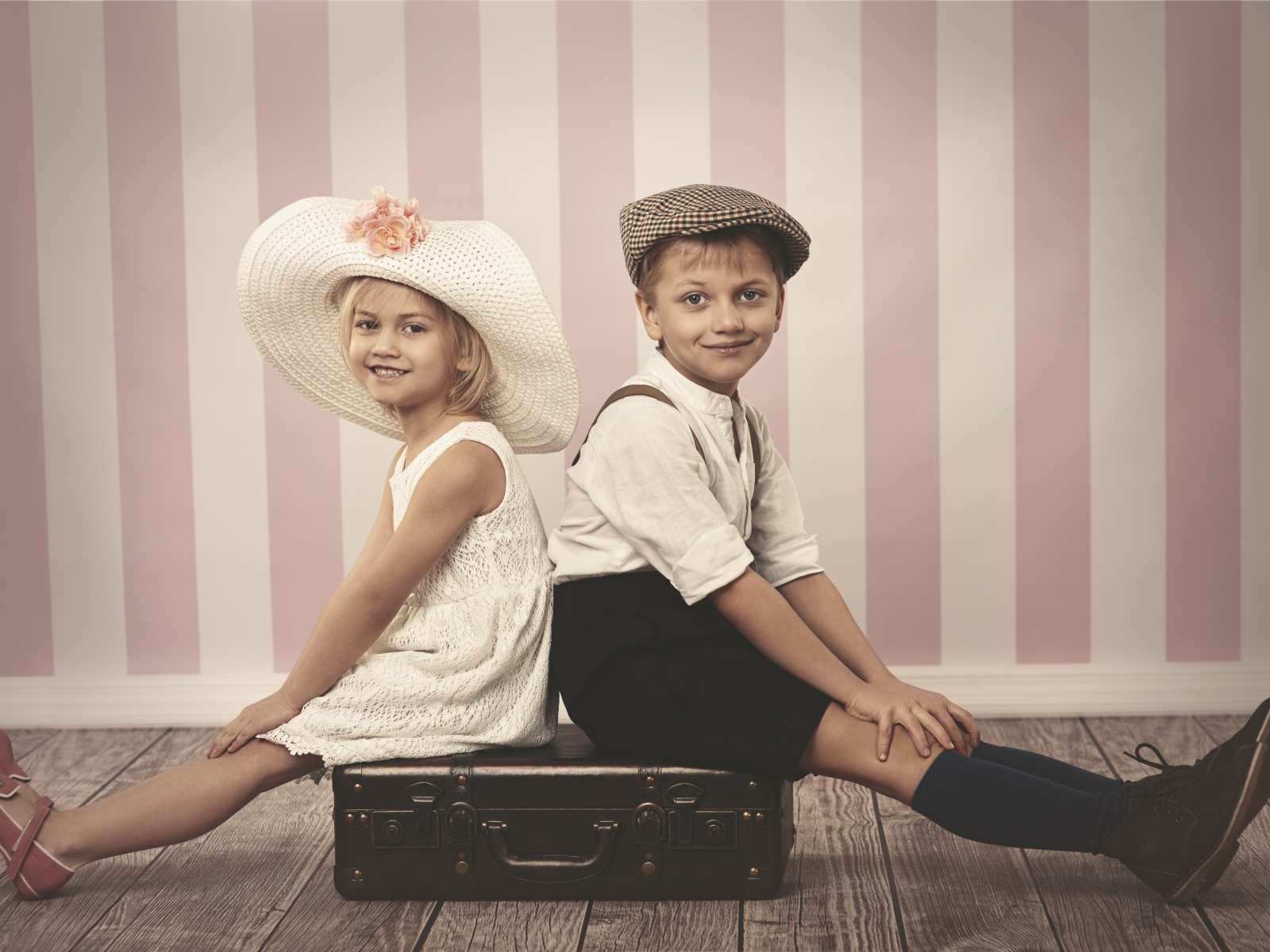 Девочка в большой белой шляпе и мальчик сидят на чемодане