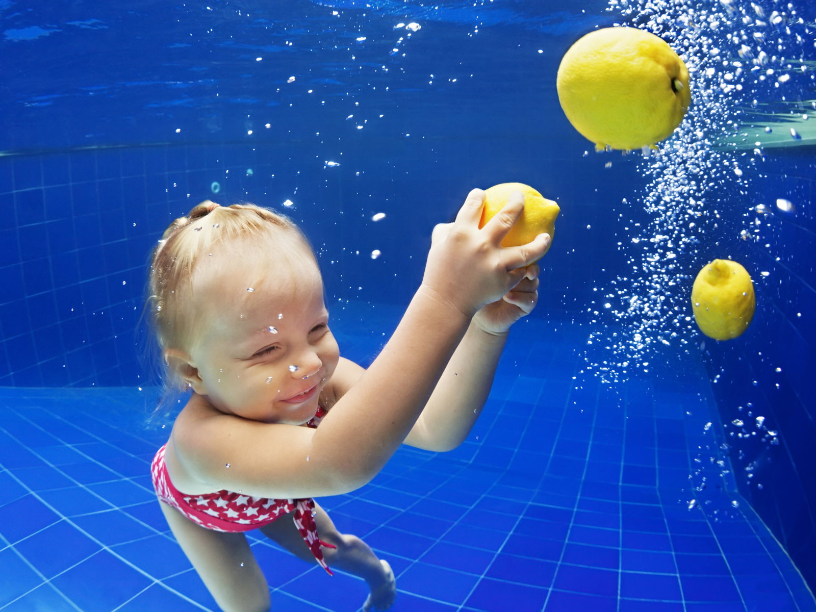 Маленькая девочка плавает в бассейне с желтыми лимонами
