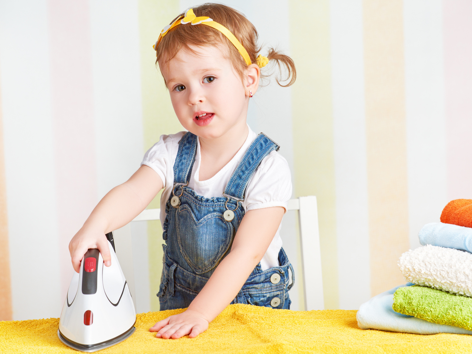 Маленькая девочка с утюгом гладит полотенце