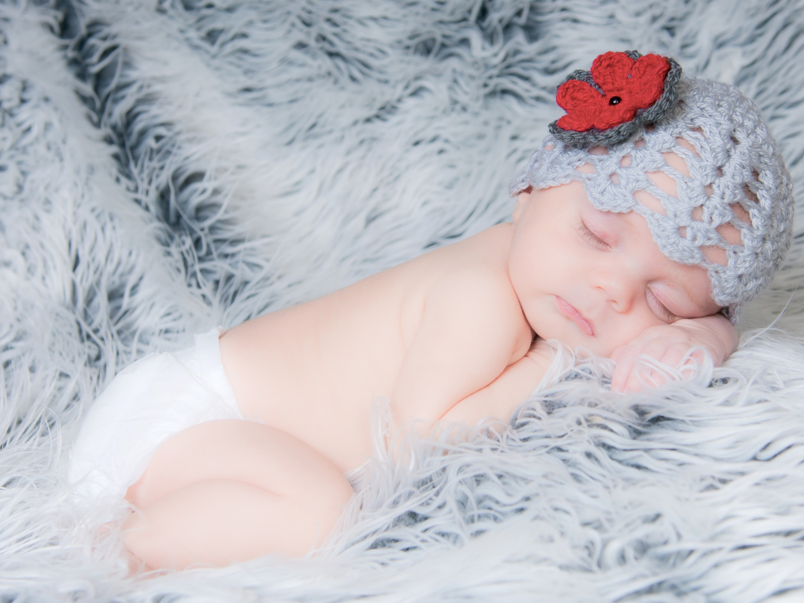 Спящий грудной ребенок в вязаной шапке с красным цветком на голове