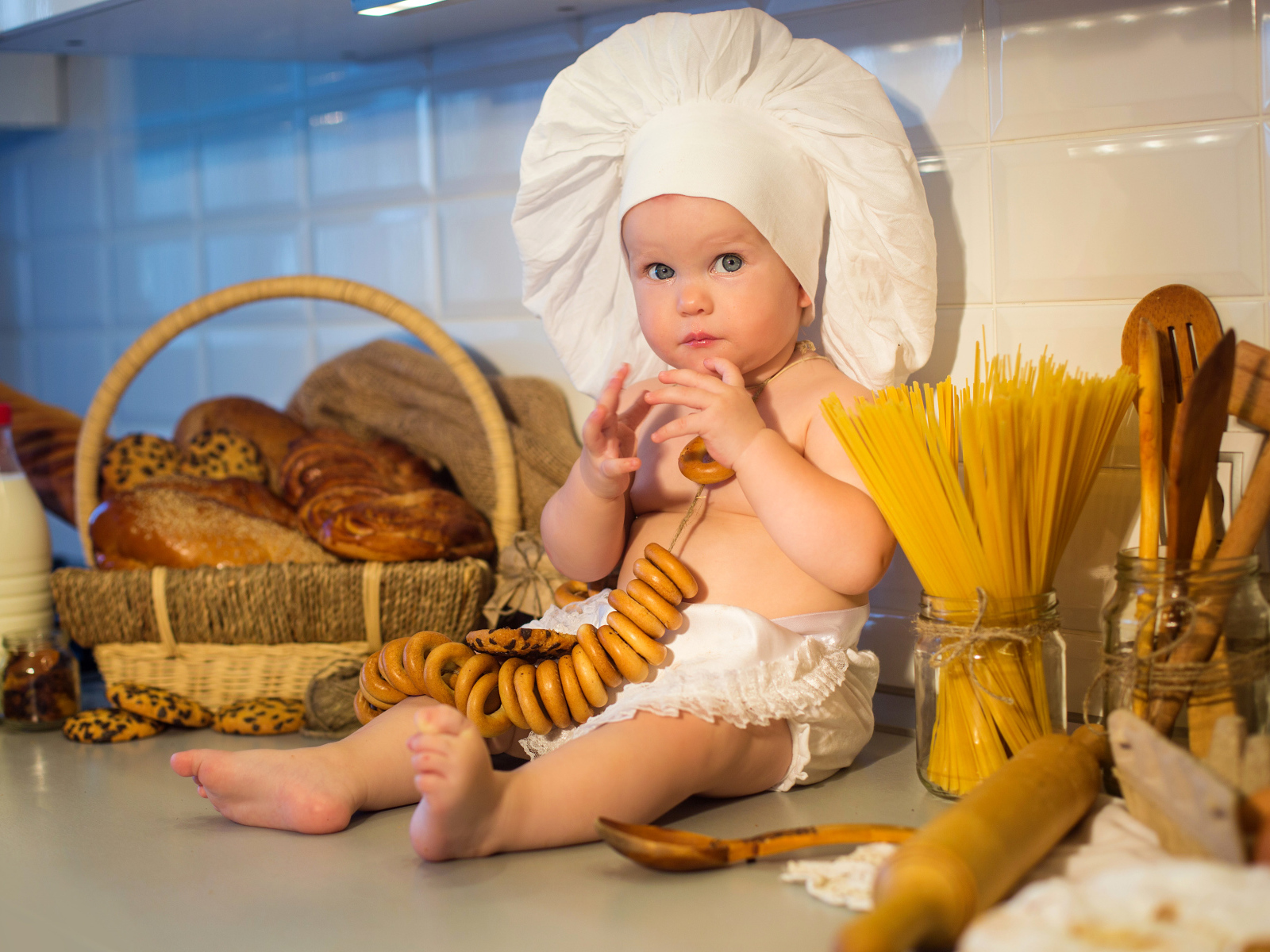 Маленький ребенок в шапке повара сидит на столе с выпечкой