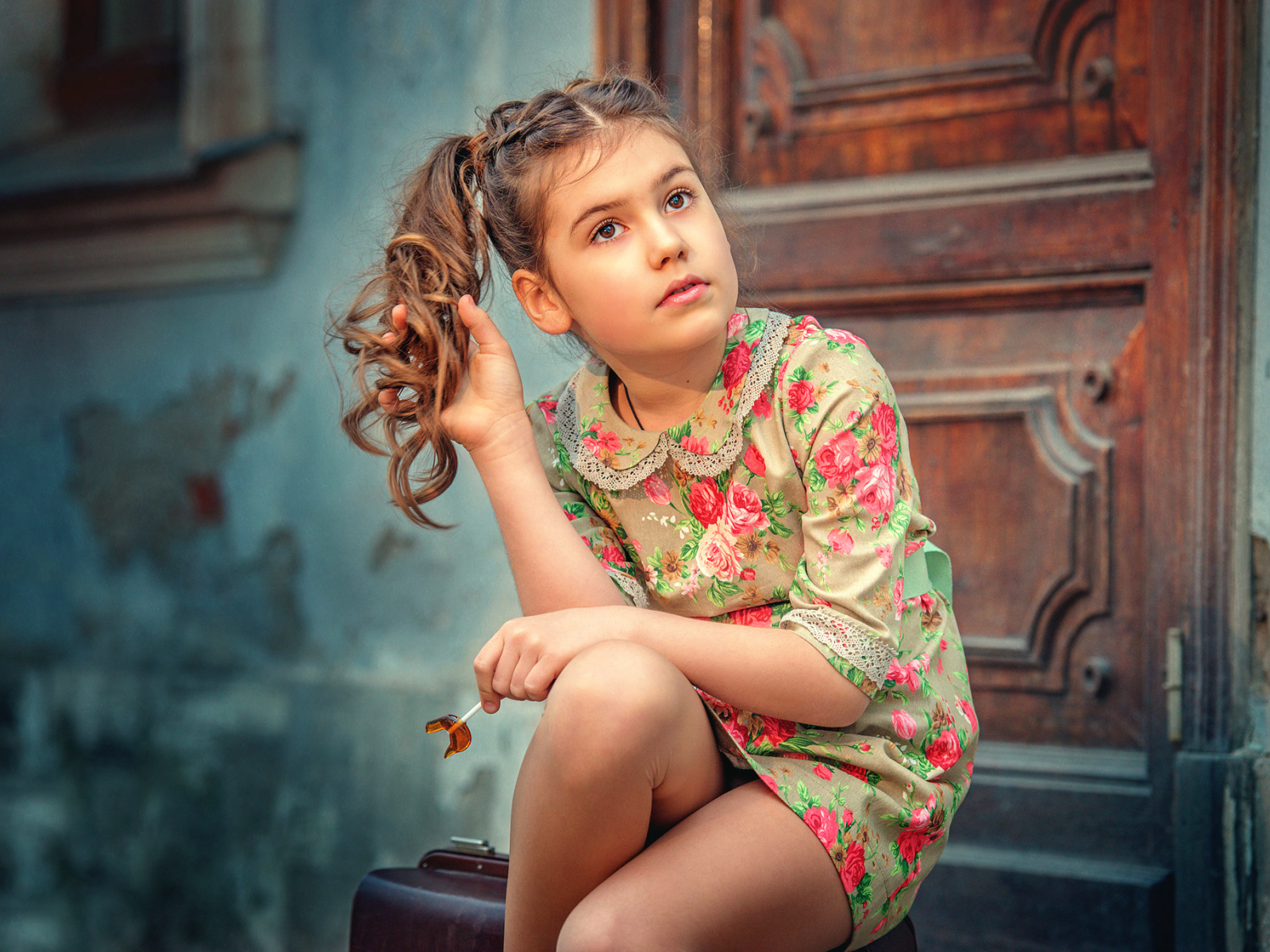 Кареглазая девочка в цветастом платье сидит на пороге
