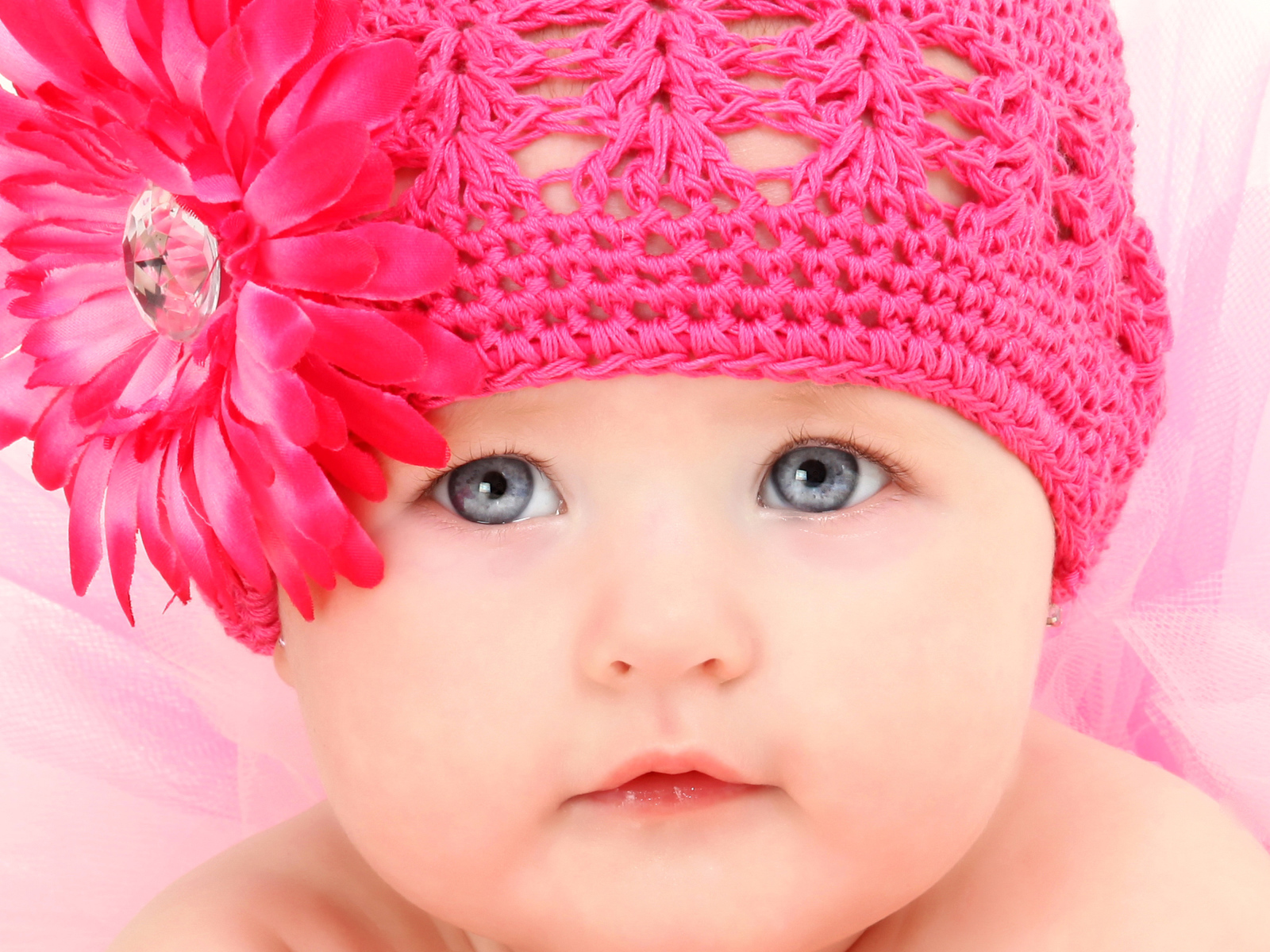 Милая голубоглазая малышка в розовой шапке с цветком герберы