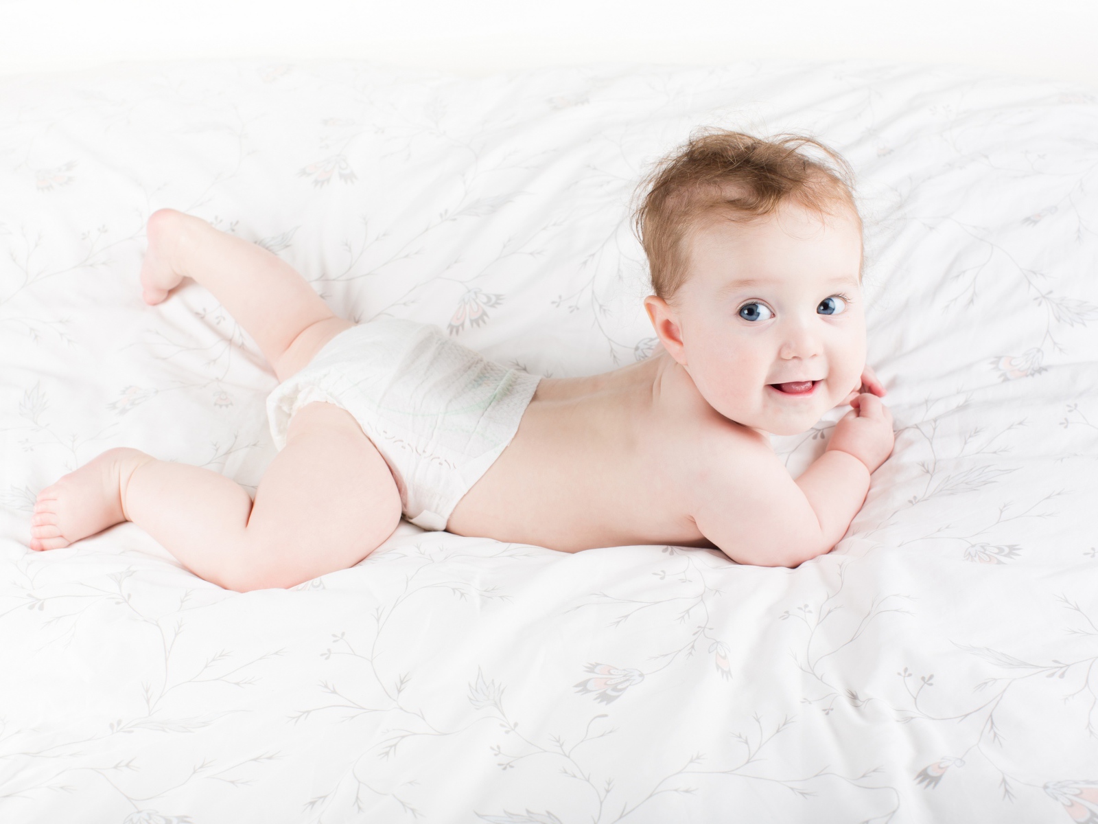Забавный голубоглазый малыш лежит на белом покрывале