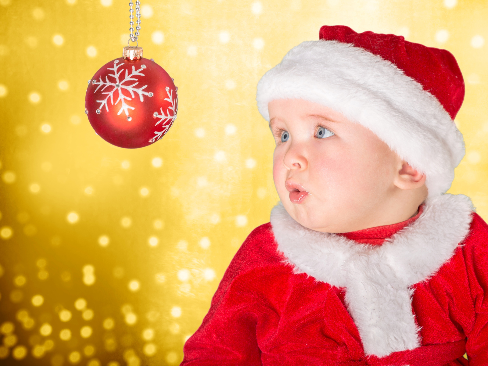 Маленький грудной ребенок в костюме Санты смотрит на елочный шар