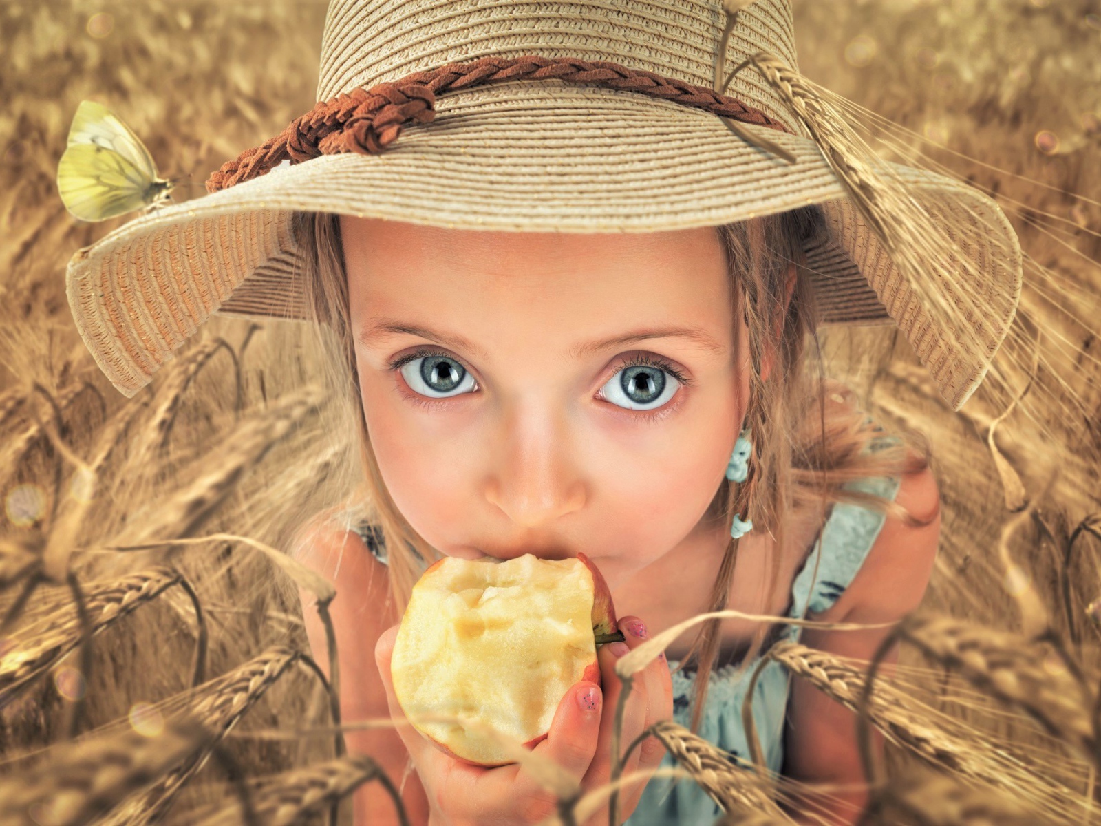 Маленькая голубоглазая девочка в шляпе ест яблоко