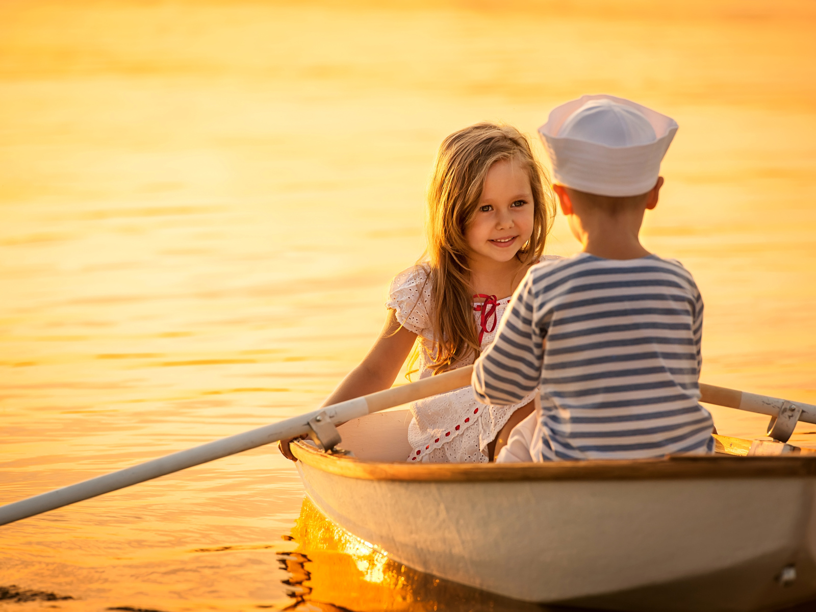 Маленькие мальчик и девочка плывут в лодке на закате солнца