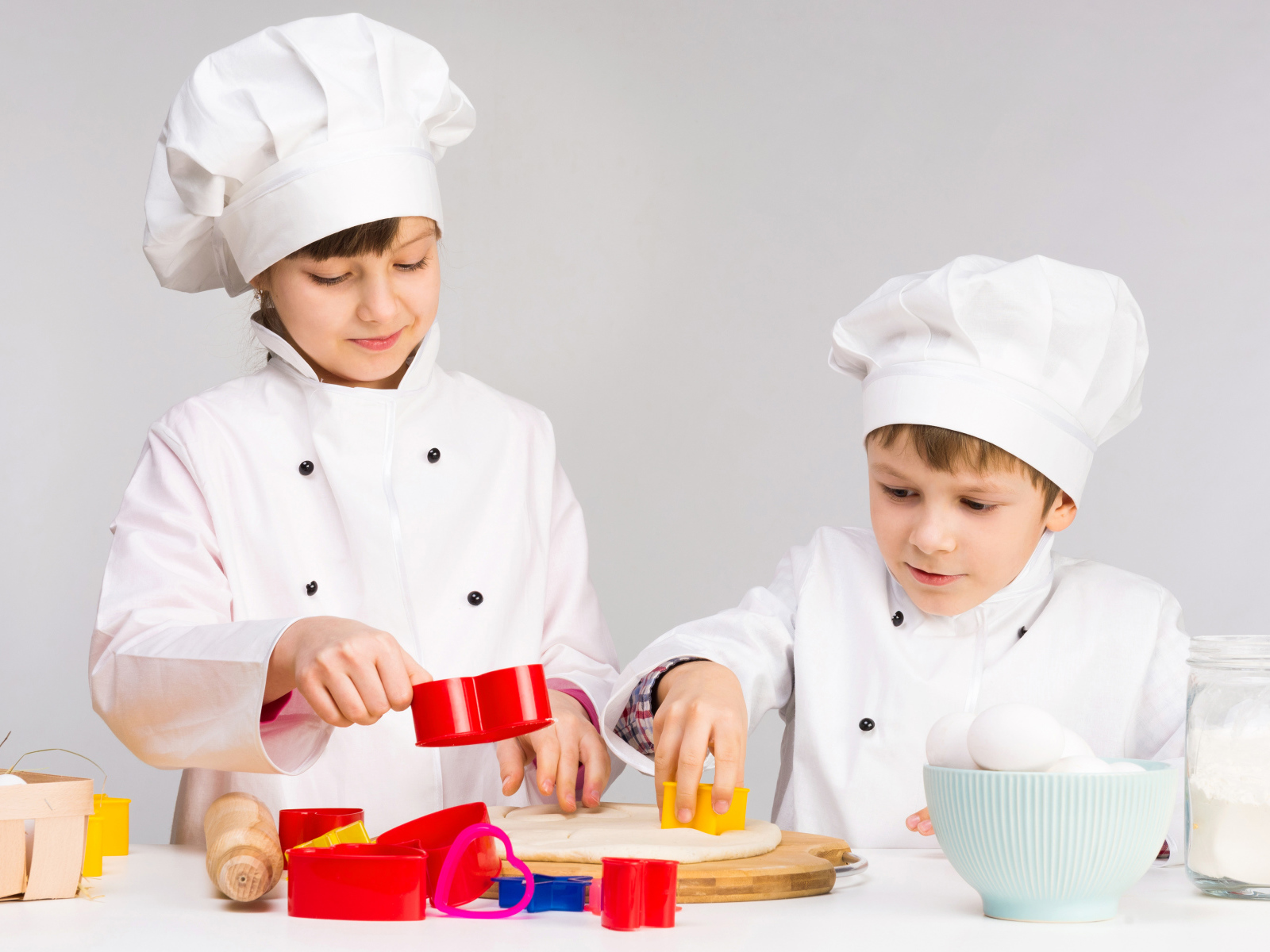 Маленькие мальчик и девочка готовят на кухне печенье