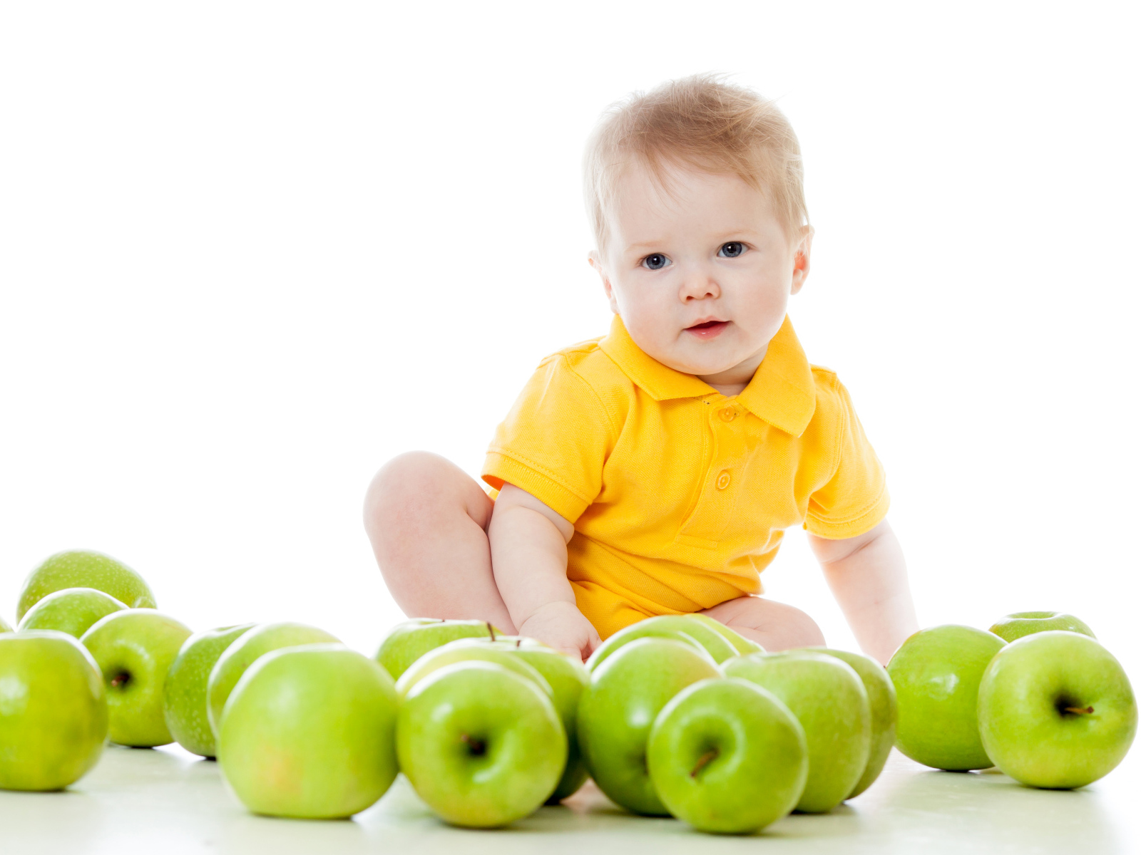Маленький мальчик с зелеными яблоками на белом фоне