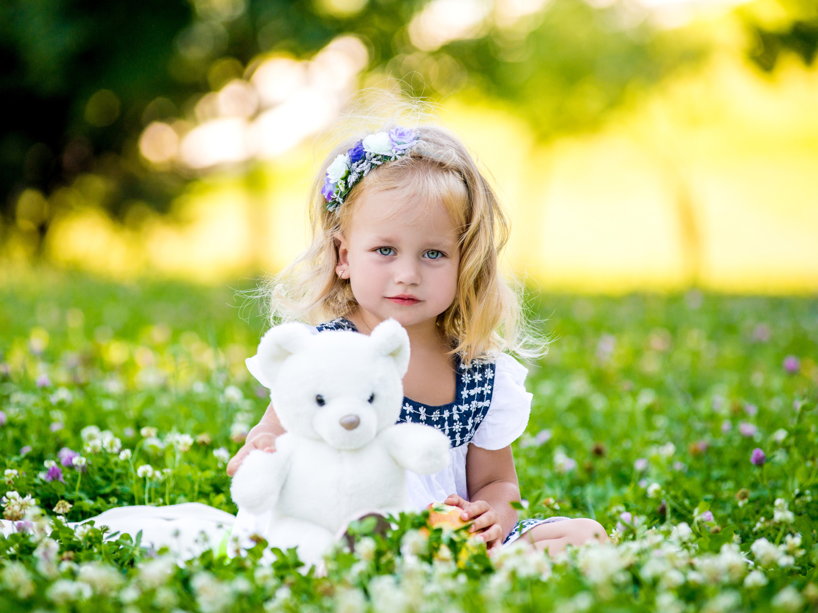 Маленькая милая девочка с игрушкой сидит на зеленой траве с цветами