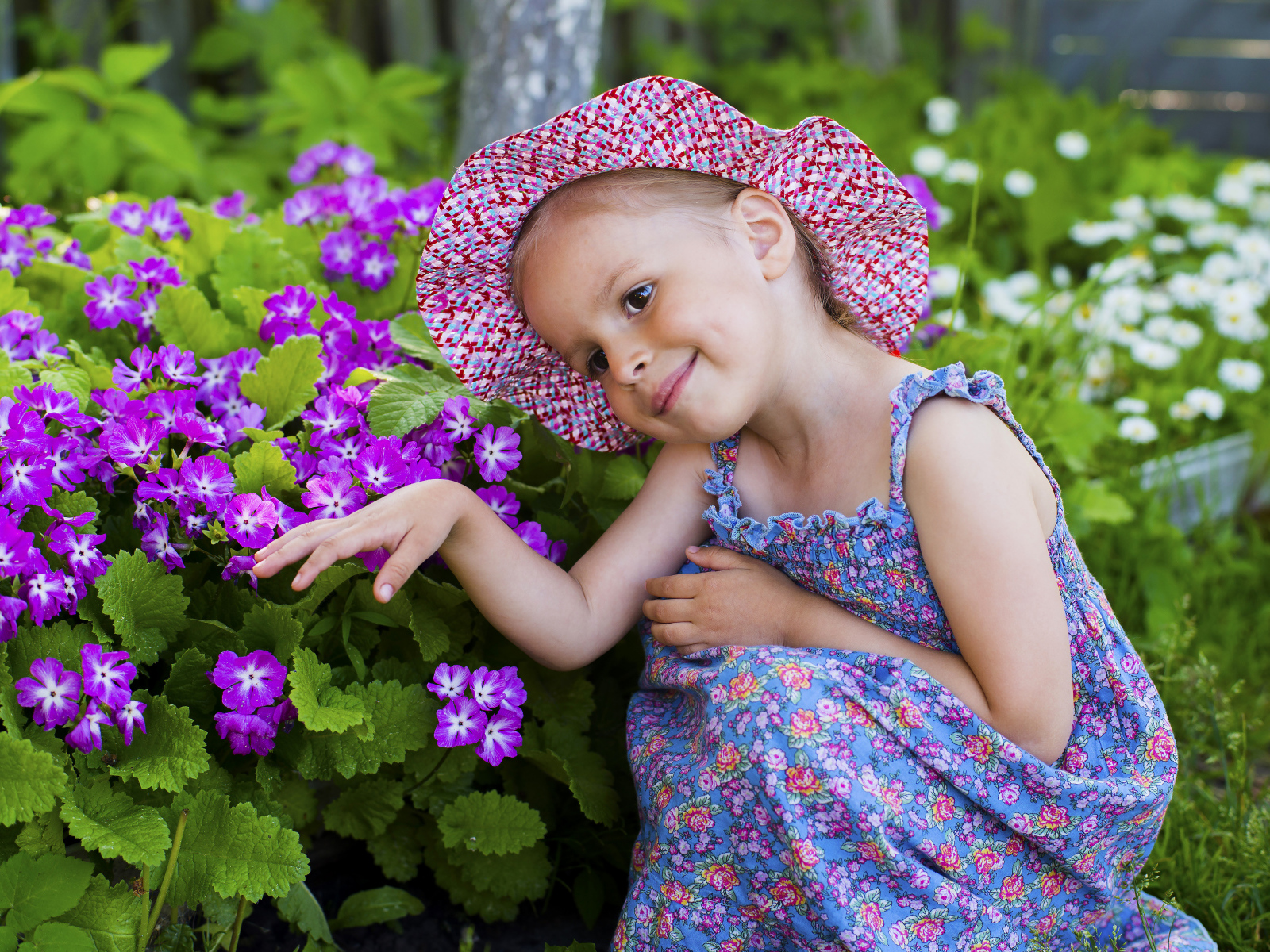 Маленькая девочка в шляпе рядом с фиолетовыми цветами