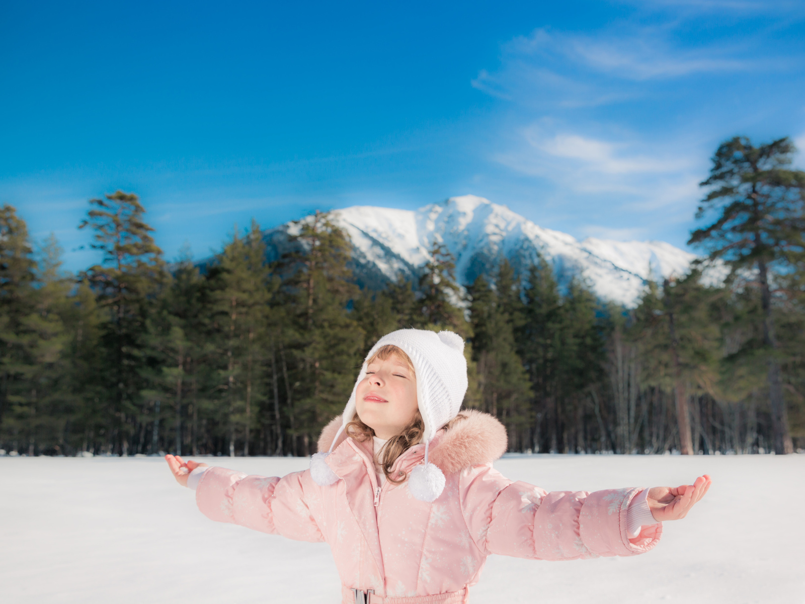 Маленькая девочка в розовой куртке на фоне гор зимой