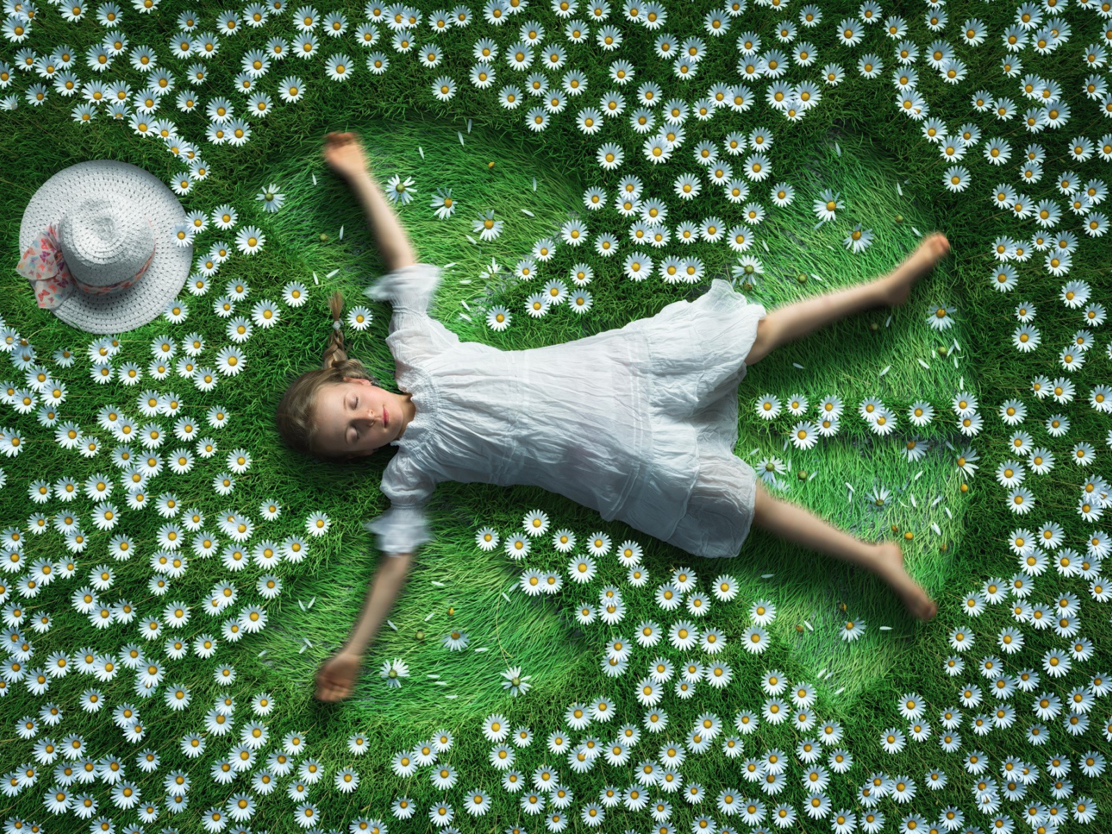 Маленькая девочка в белом платье лежит на зеленой траве с ромашками