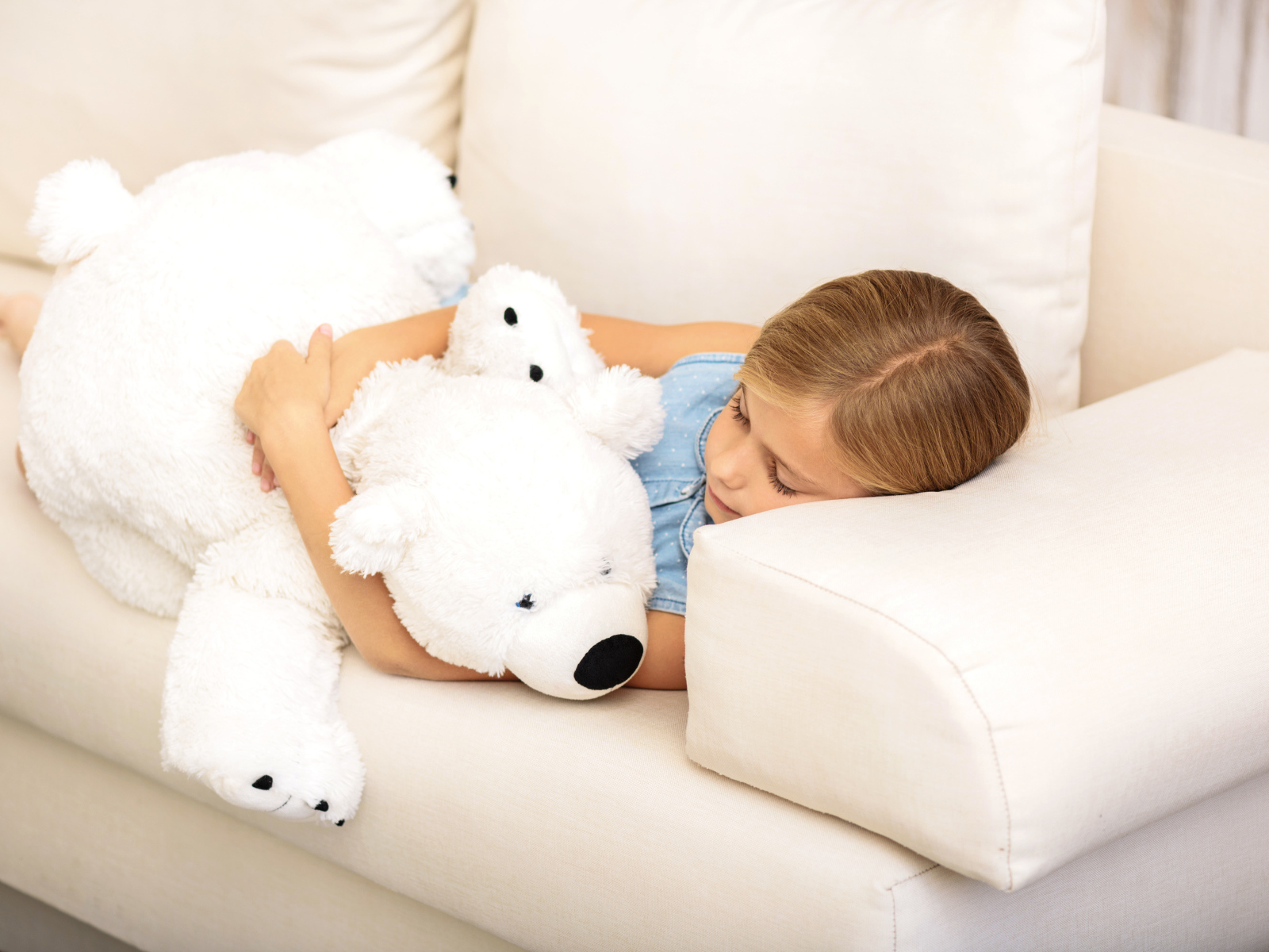 Маленькая девочка спит с белым плюшевым мишкой на диване