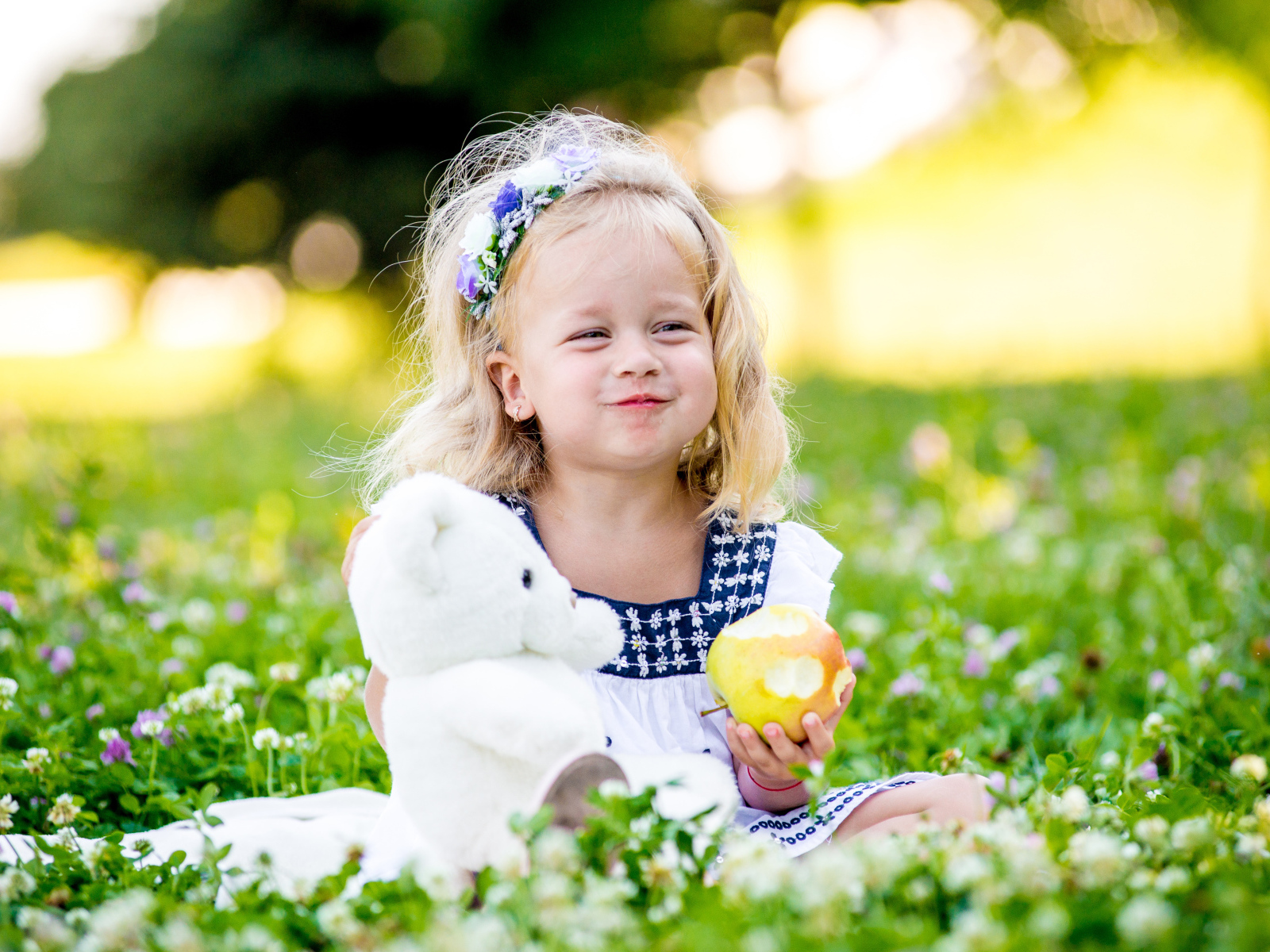 Маленькая девочка с белым медвежонком в руках и большим яблоком