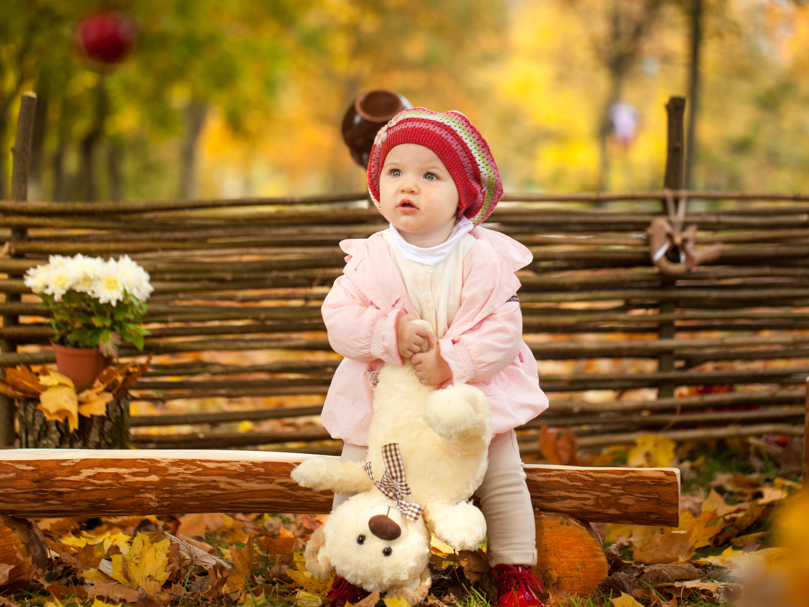 Маленькая девочка с плюшевым мишкой сидит на деревянной лавке осенью