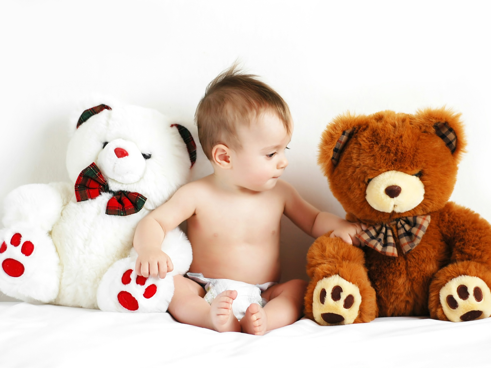 Младенец сидит с двумя большими плюшевыми медведями