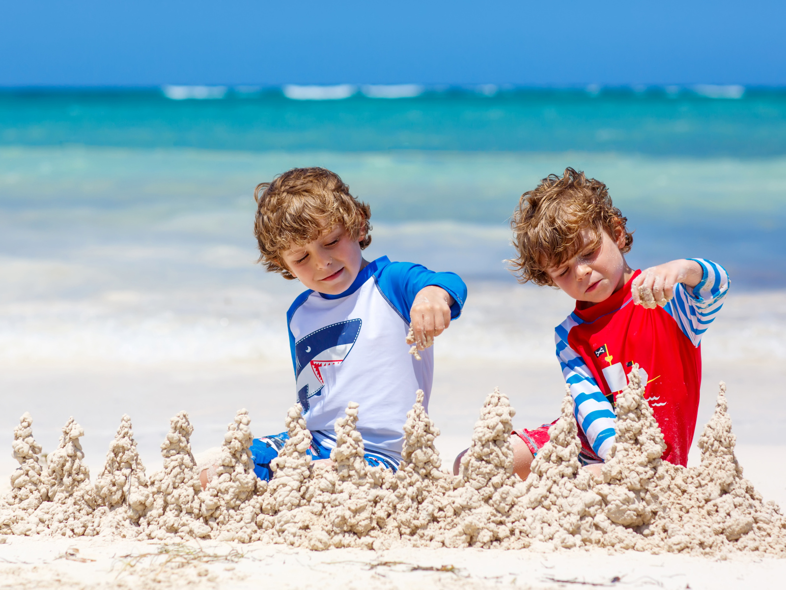 Два маленьких мальчика играют с песком на пляже