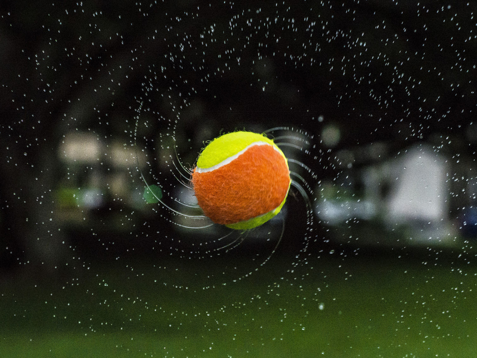 Теннисный мяч летит в каплях воды 