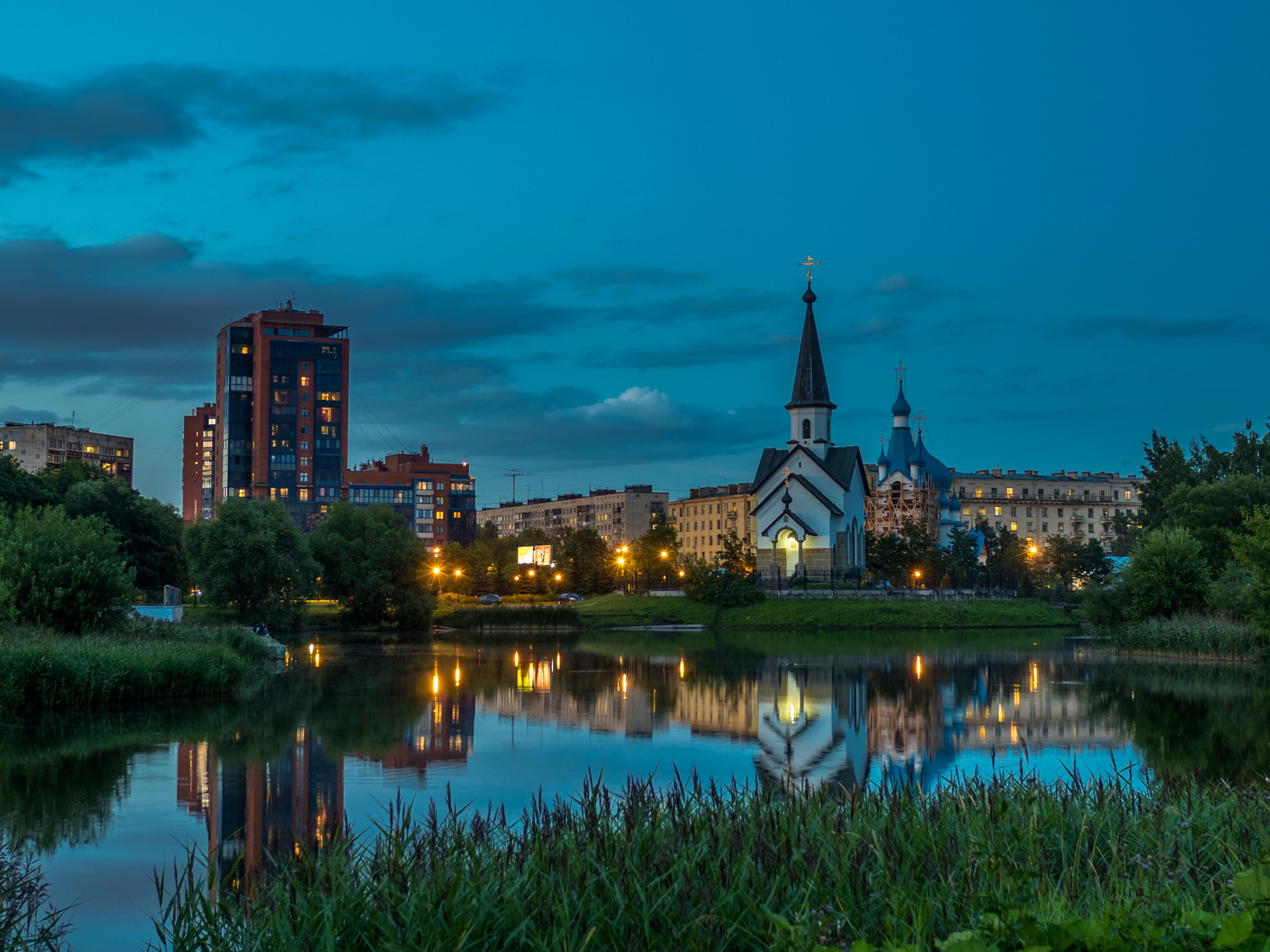 Вечерние огни маленькой церкви и домов отражаются в воде городского пруда, Санкт-Петербург. Россия