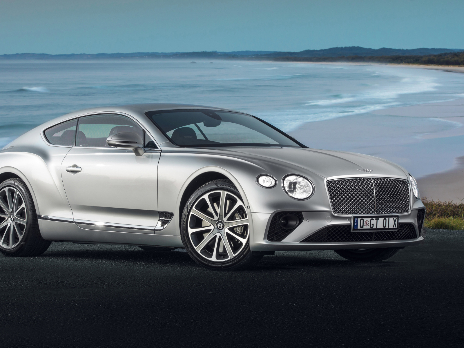 Серебристый автомобиль Bentley Continental GT 2018 года на фоне океана 