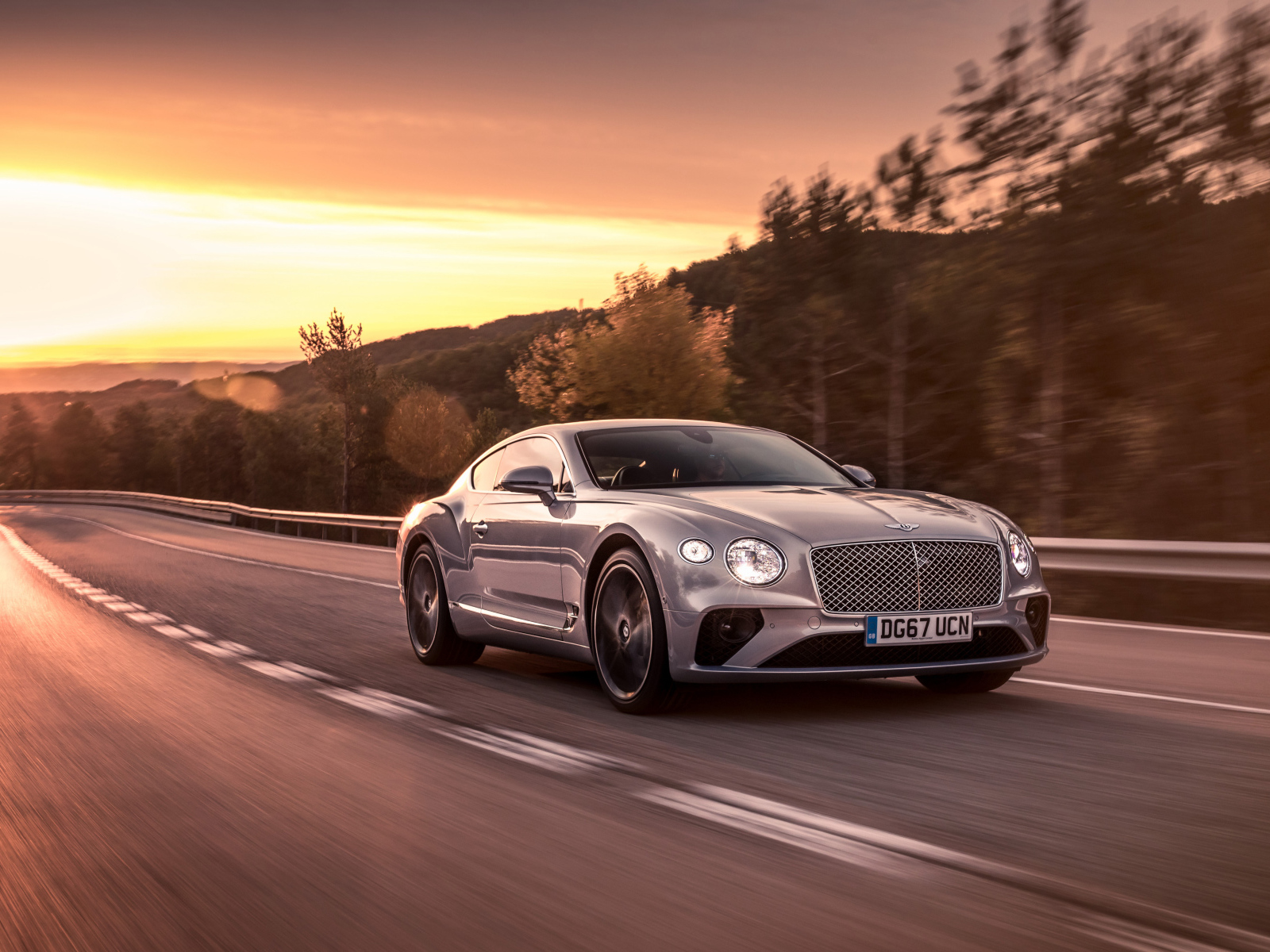 Серебристый автомобиль Bentley Continental GT 2018 года на фоне заката