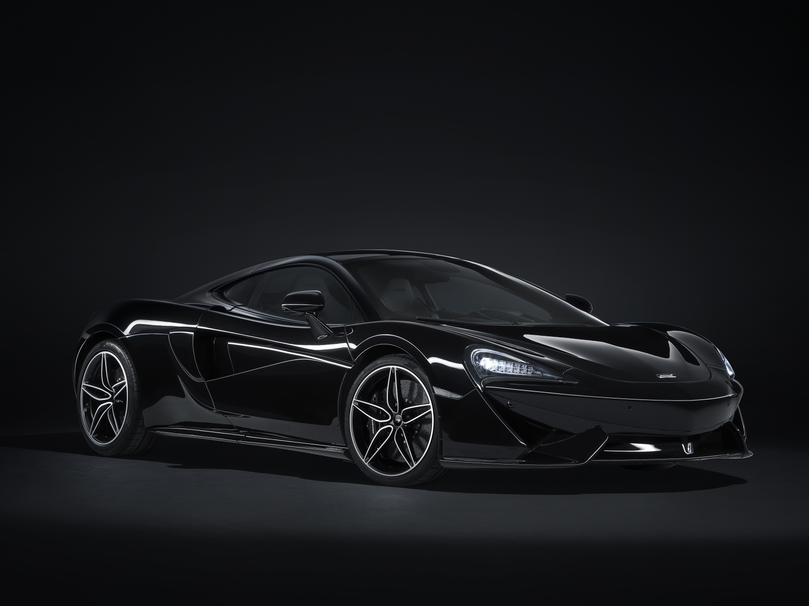 Черный спортивный автомобиль McLaren 570GT на сером фоне