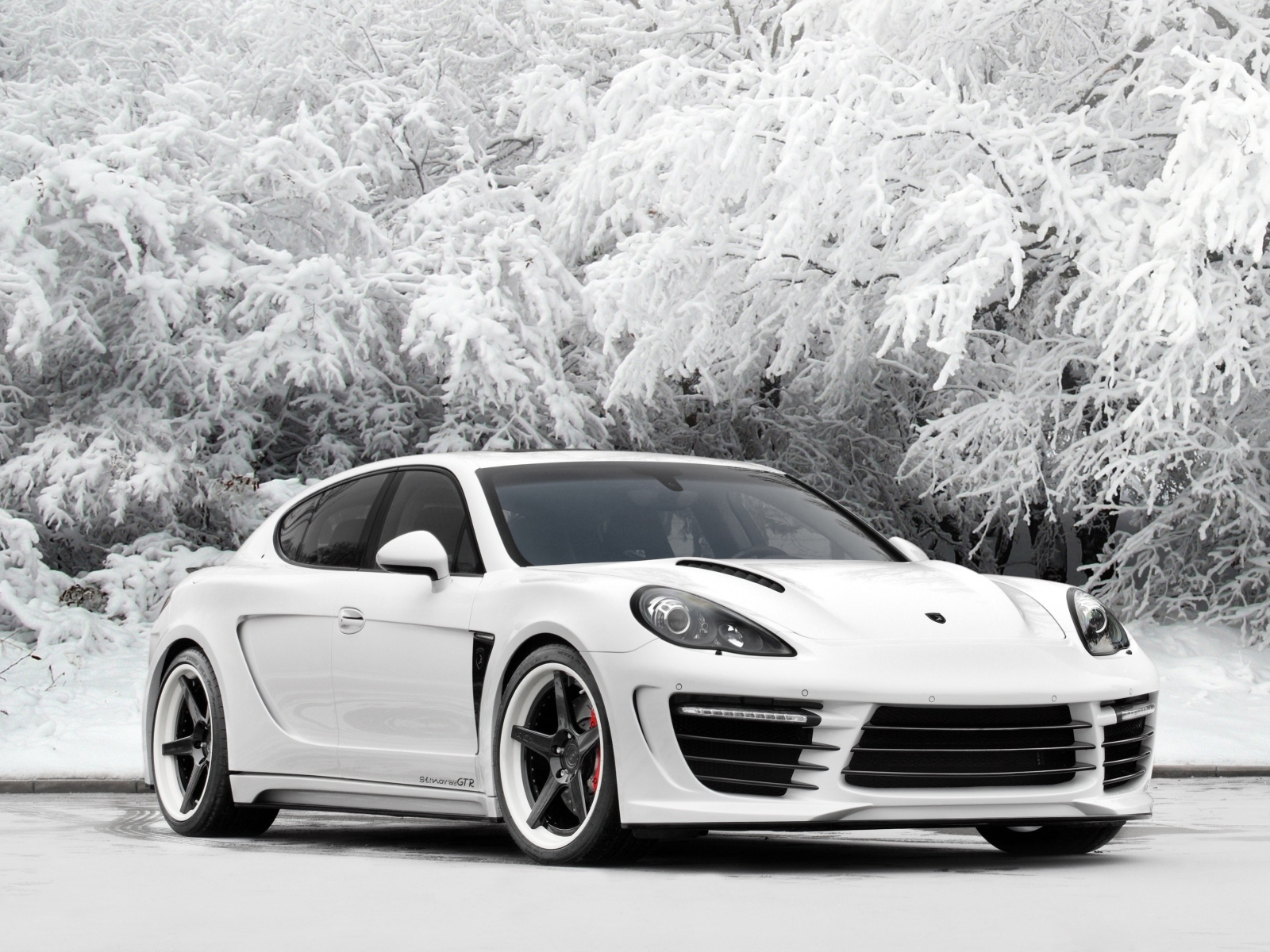 Белый автомобиль Porsche Panamera на фоне покрытых инеем деревьев 