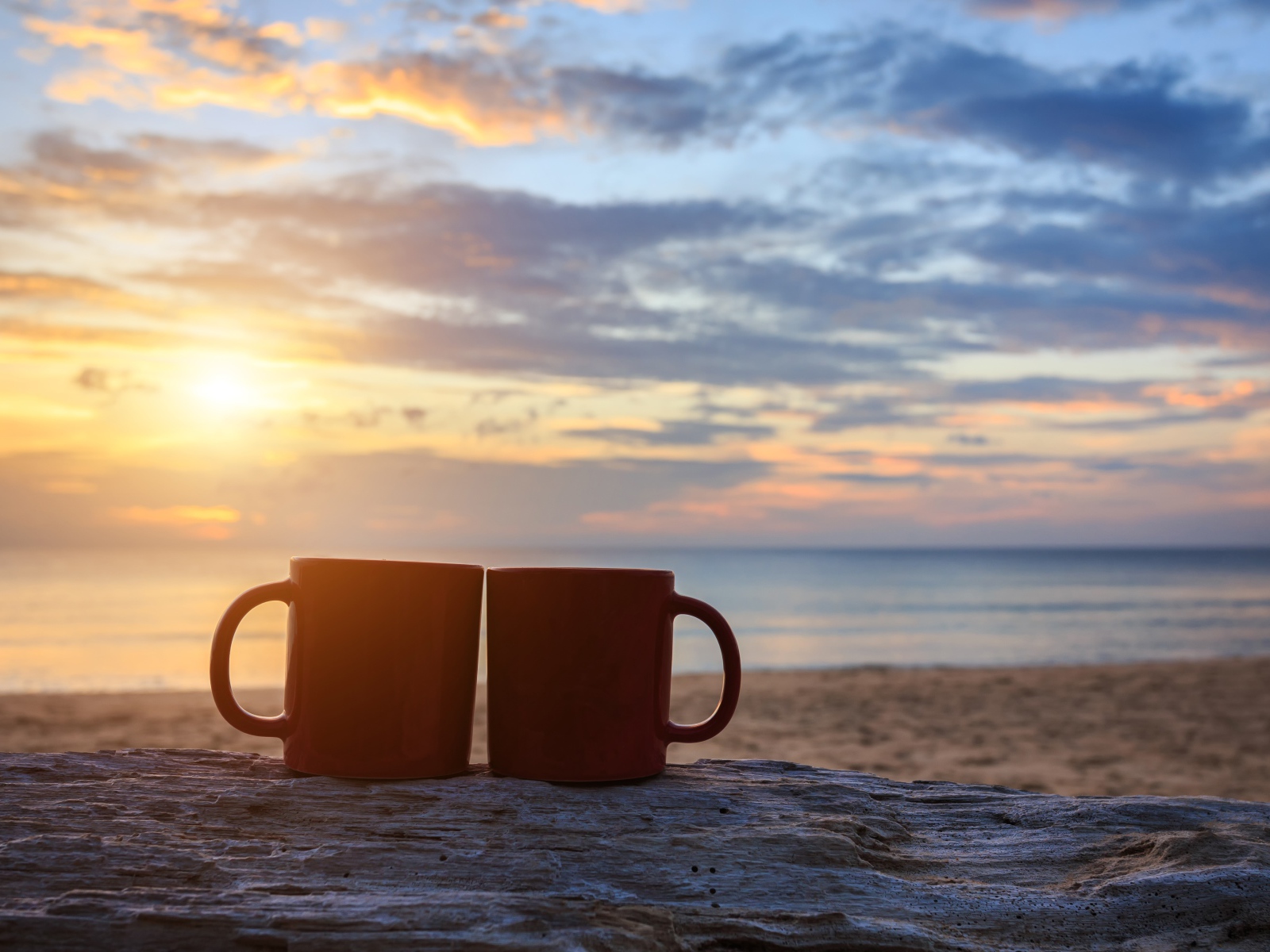 Две чашки стоят на песке на фоне рассвета 
