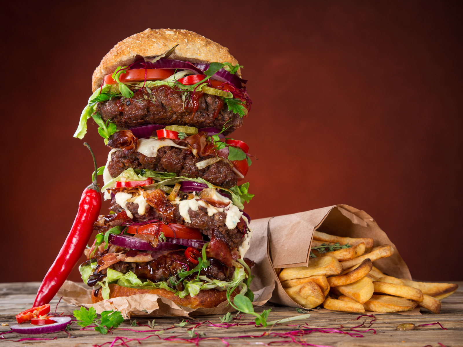 Огромный гамбургер на столе с картофелем фри и острым перцем