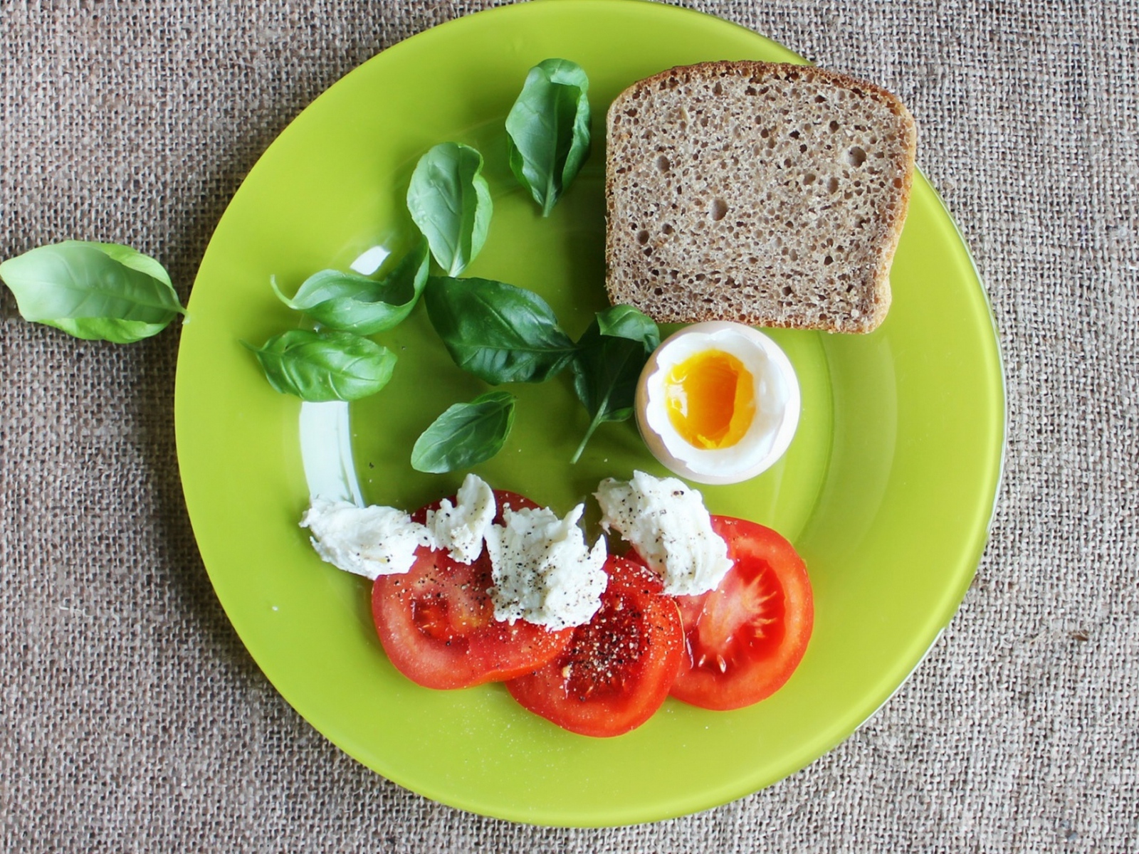 Легкий завтрак с помидорами, яйцом, кусочком хлеба и листьями базилика