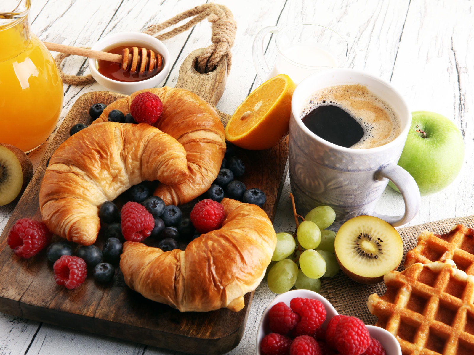Croissants with berries, on the table with coffee, honey and waffles