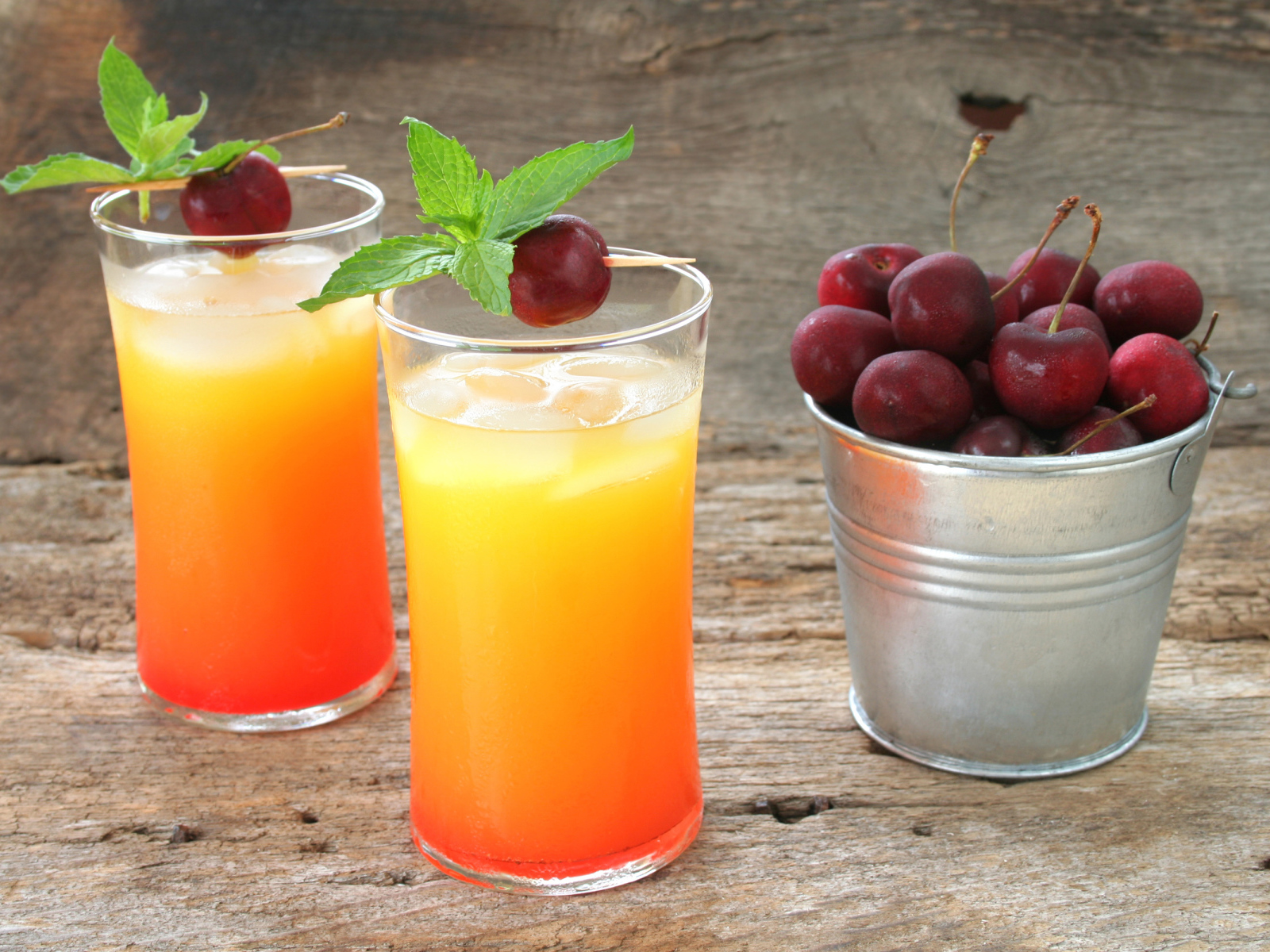 Два стакана напитка на столе с ведром с черешней
