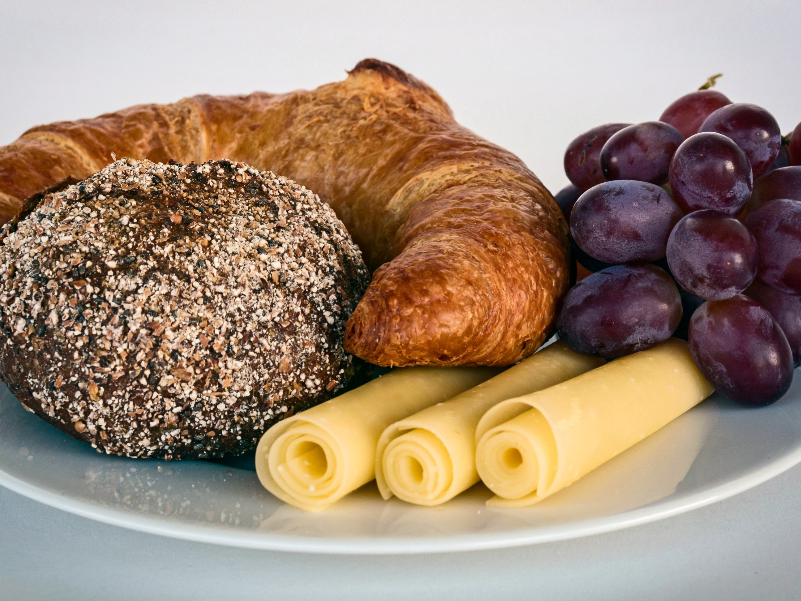 Свежая выпечка с сыром и розовым виноградом на белой тарелке 