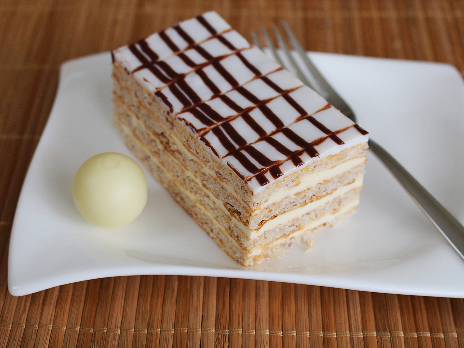 Кусок торта на белой тарелке с вилкой и конфетой 