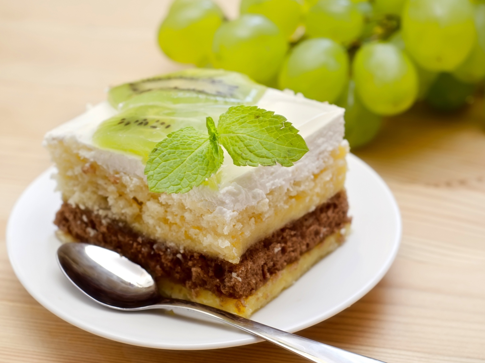 Кусок торта с киви и мятой на столе с виноградом