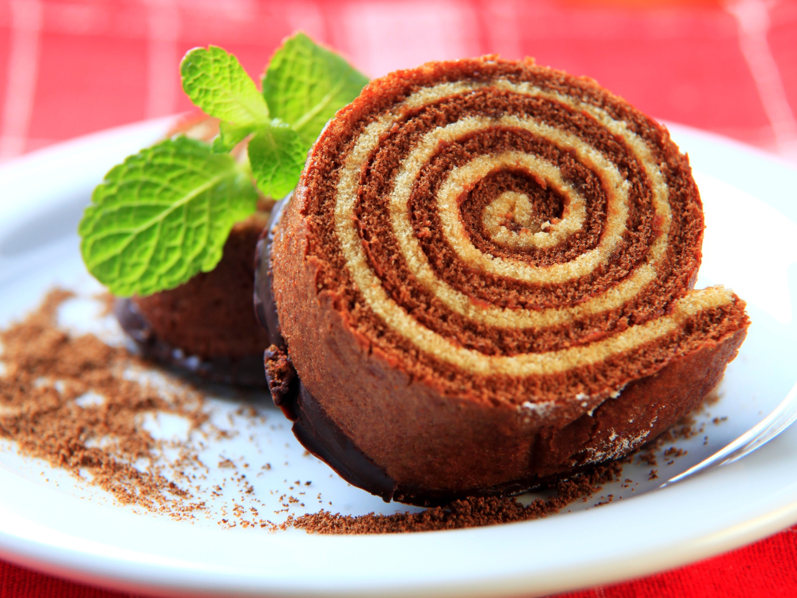 Кусок сладкого рулета с шоколадом и листом мяты на тарелке