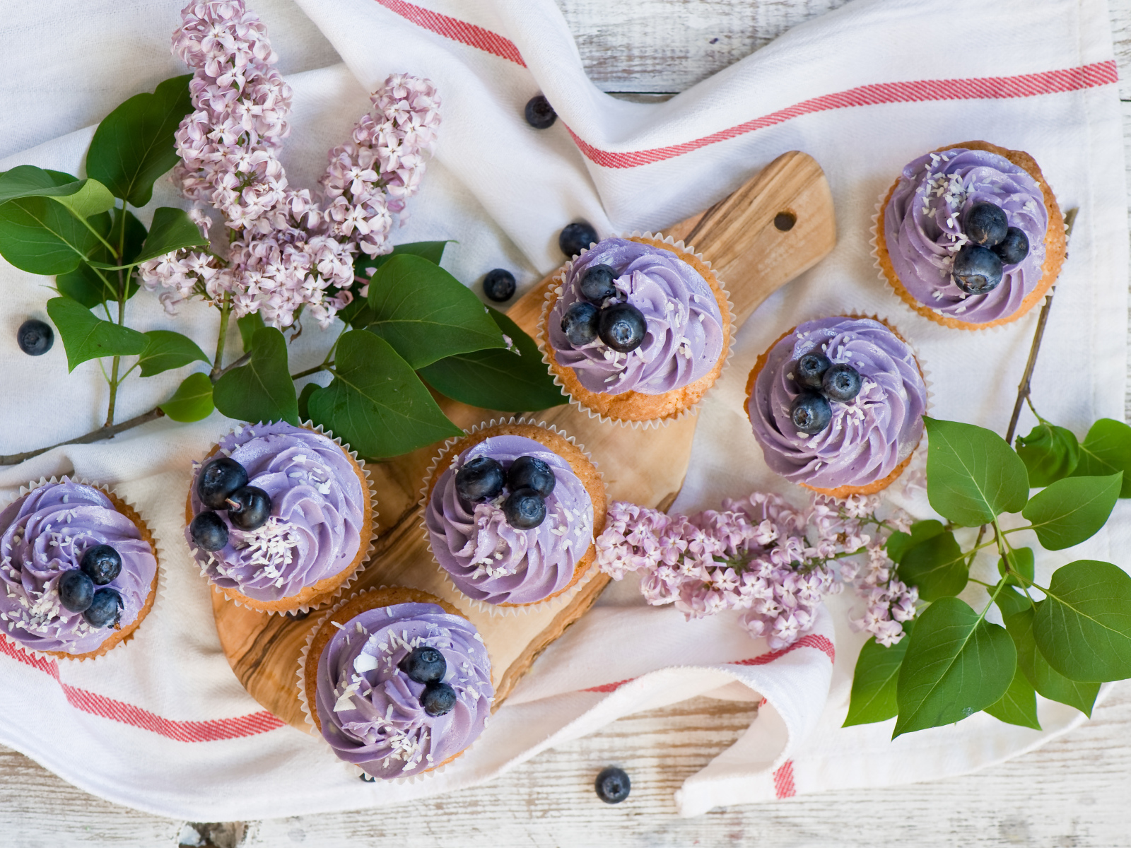 Кексы с кремом и ягодами черники на столе с ветками сирени 