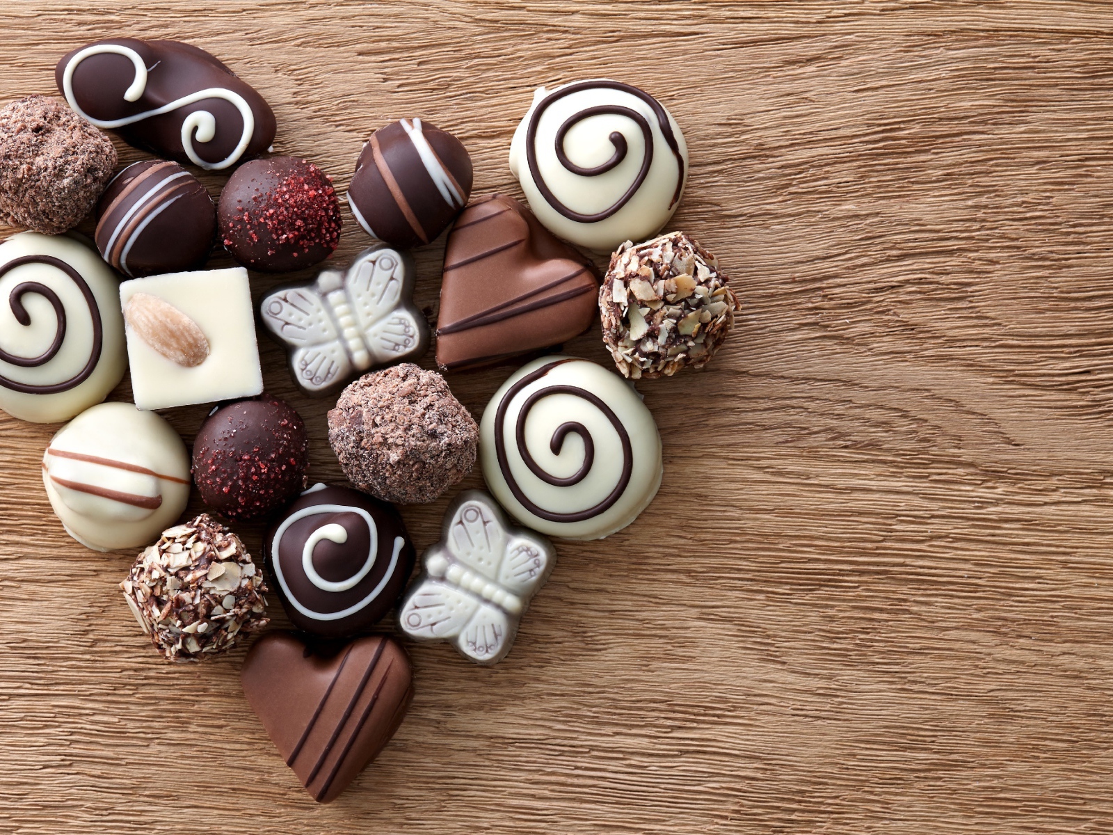 Сердце из шоколадных конфет ассорти на деревянном столе