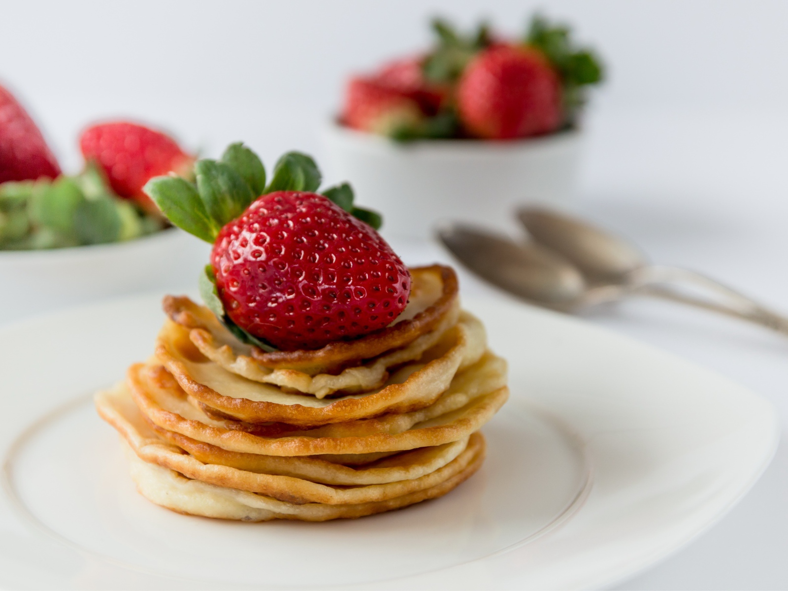 Оладьи с ягодами свежей клубники на белой тарелке 