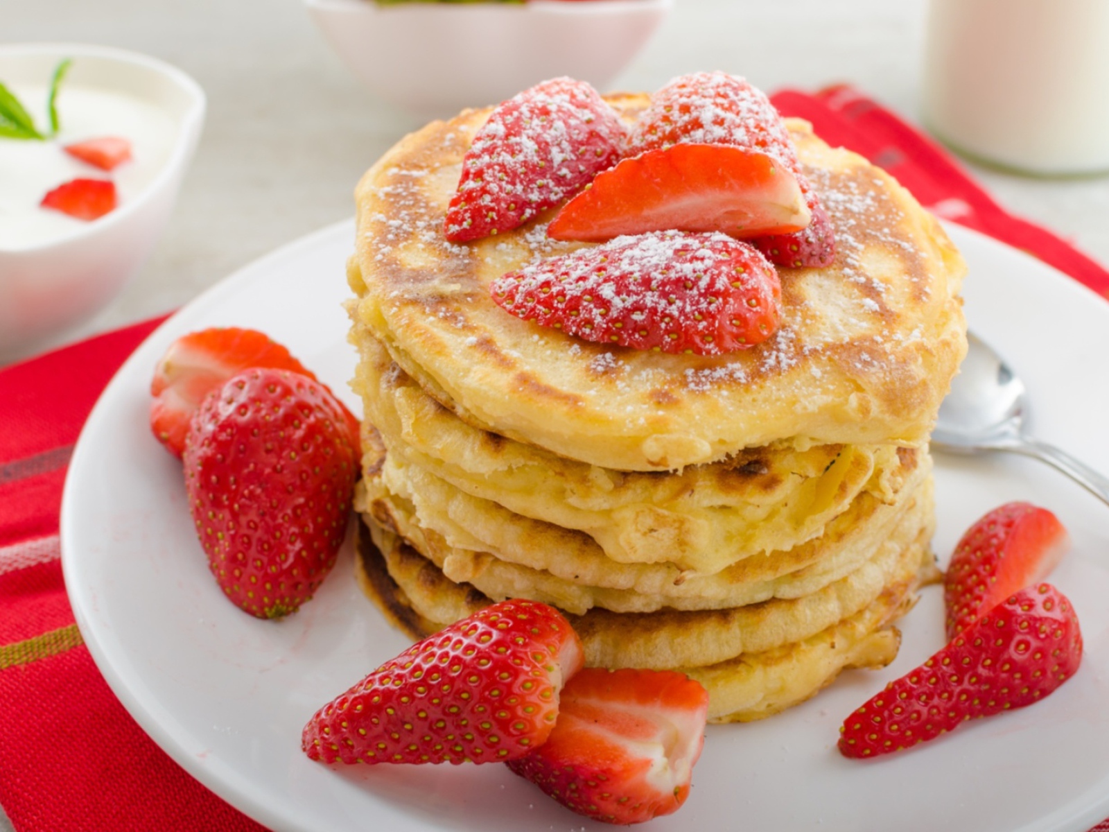 Оладьи с клубникой и сахарной пудрой на белой тарелке 