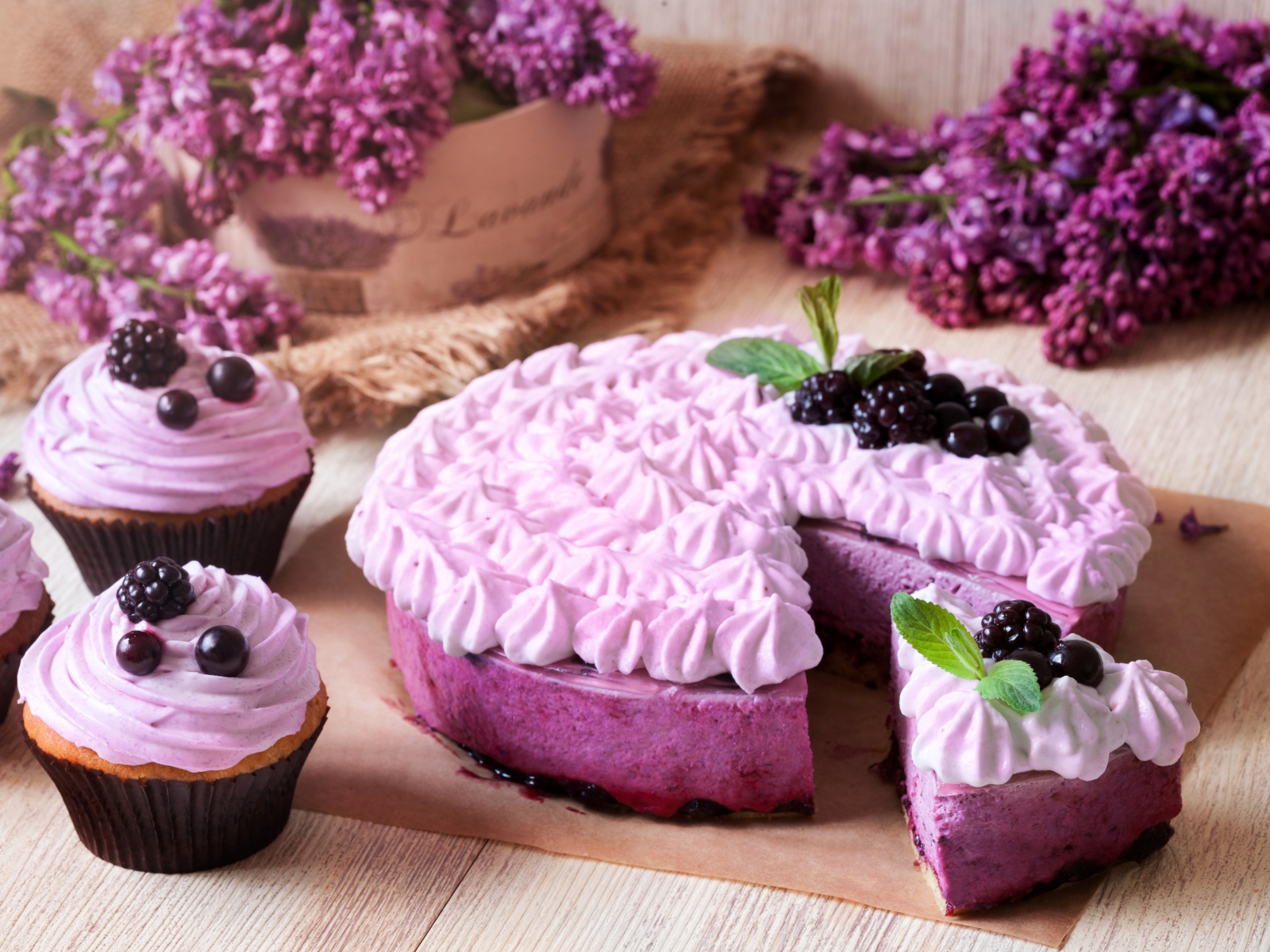 Пирог с кремом и вкусными кексами с черникой на столе с цветами сирени