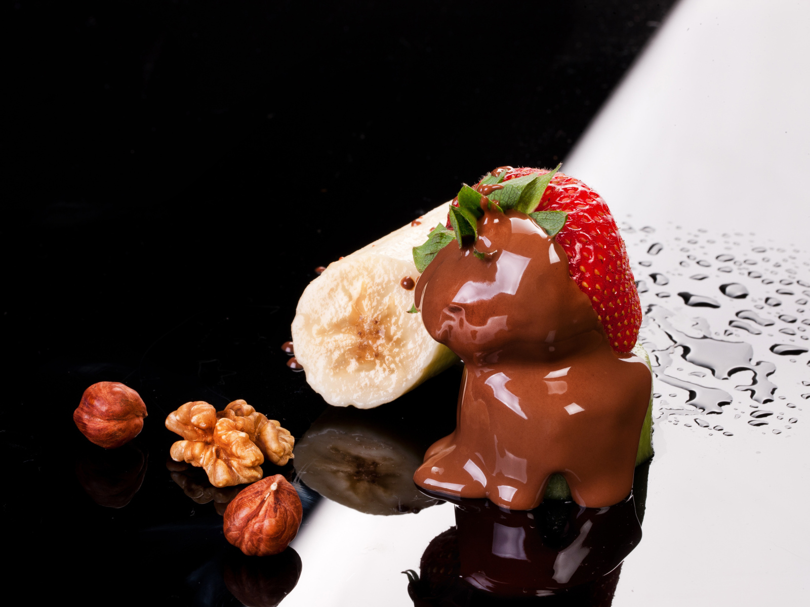 Клубника в шоколаде, банан и орехи на черной поверхности