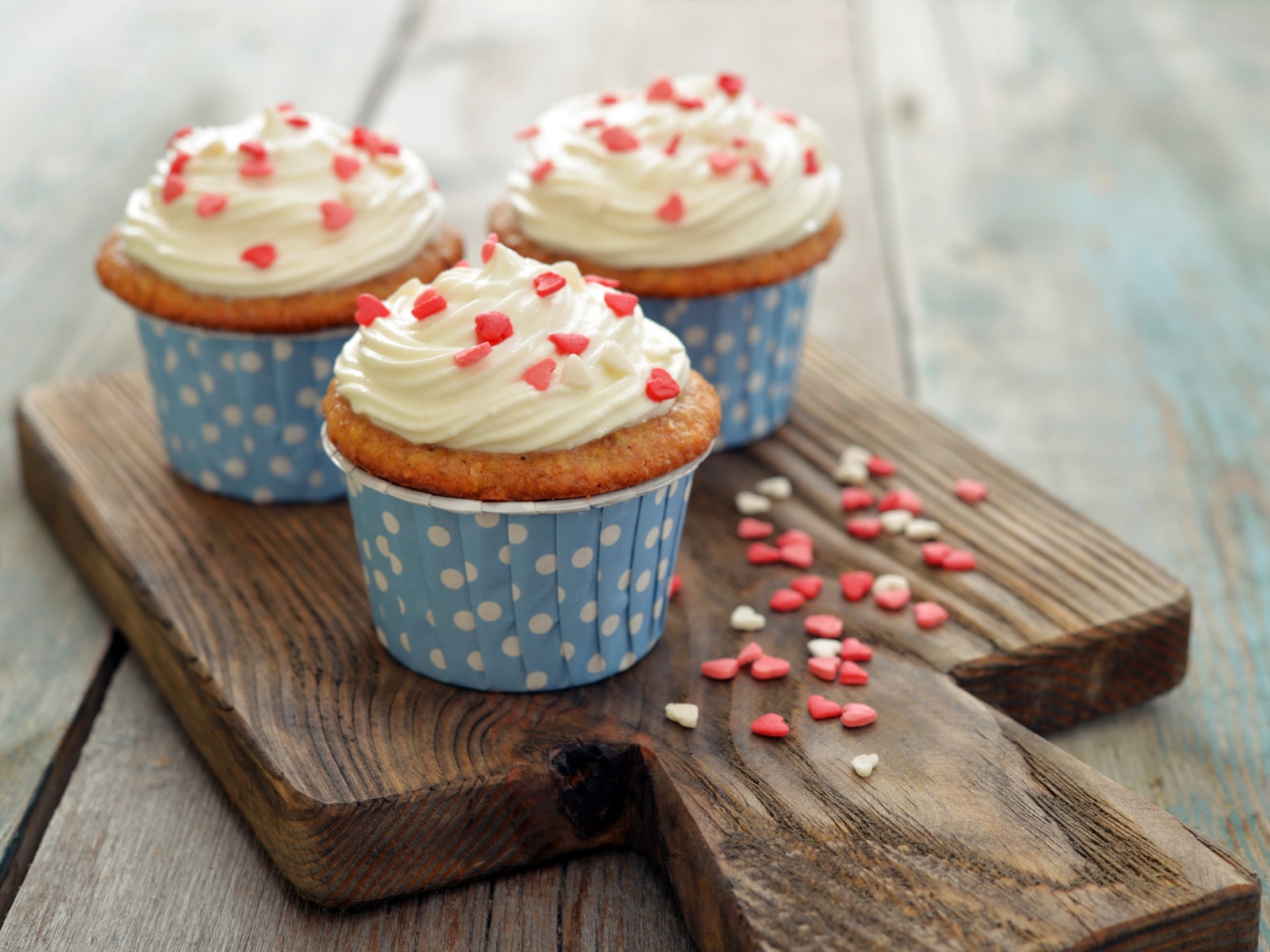 Три кекса со сливками украшены сердечками стоят на разделочной доске