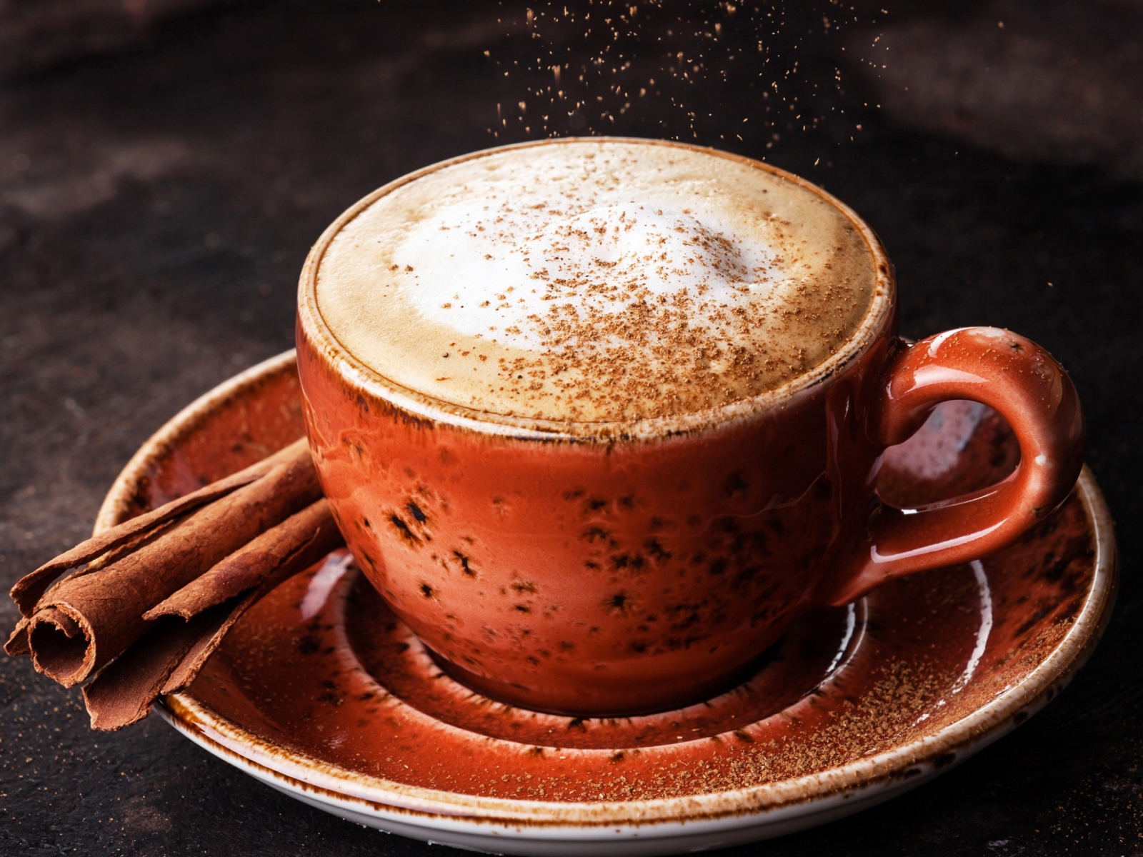 Чашка кофе с пенкой на блюдце с корицей