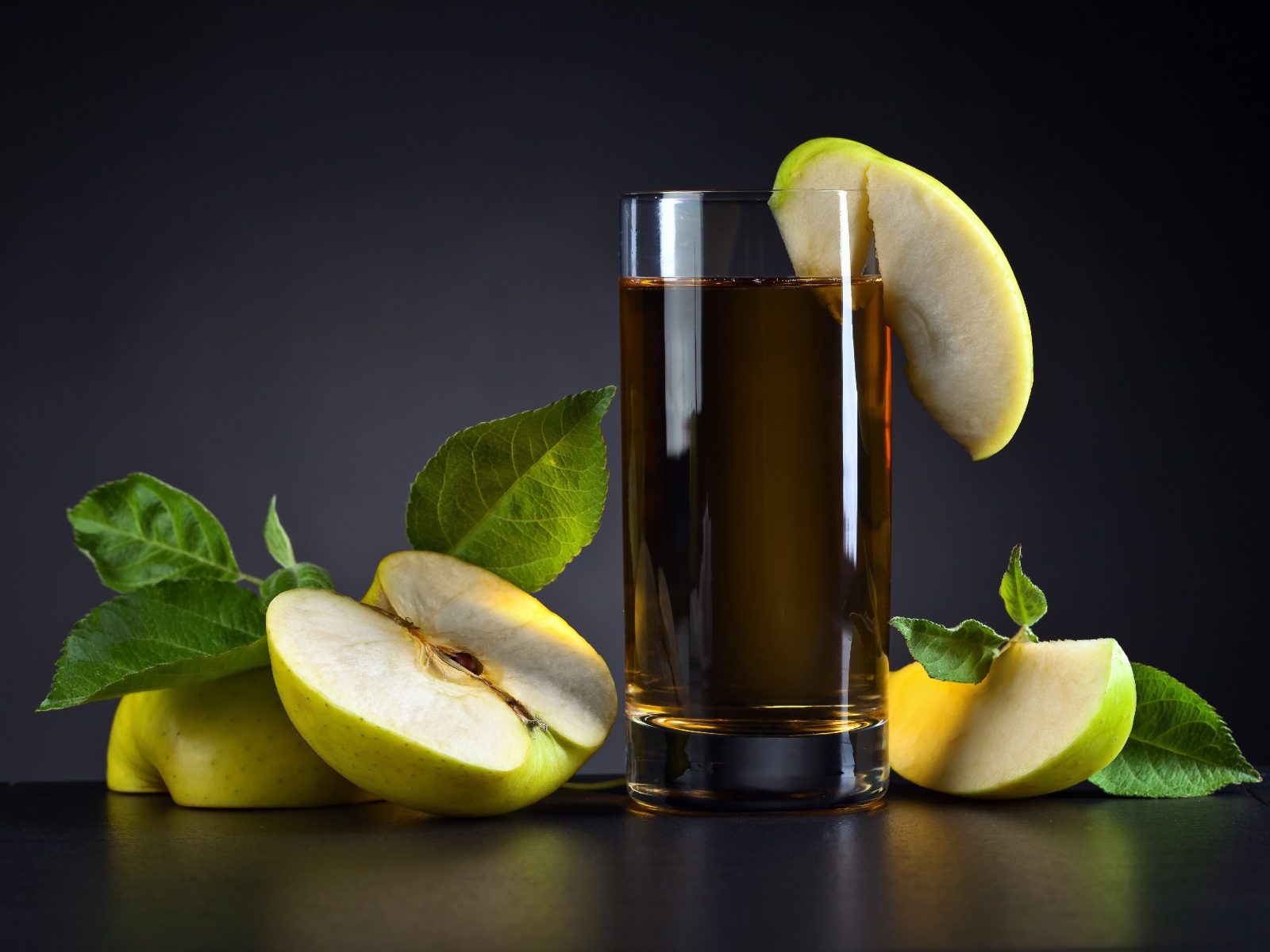 Яблочный сок в стакане на столе со свежими яблоками на сером фоне