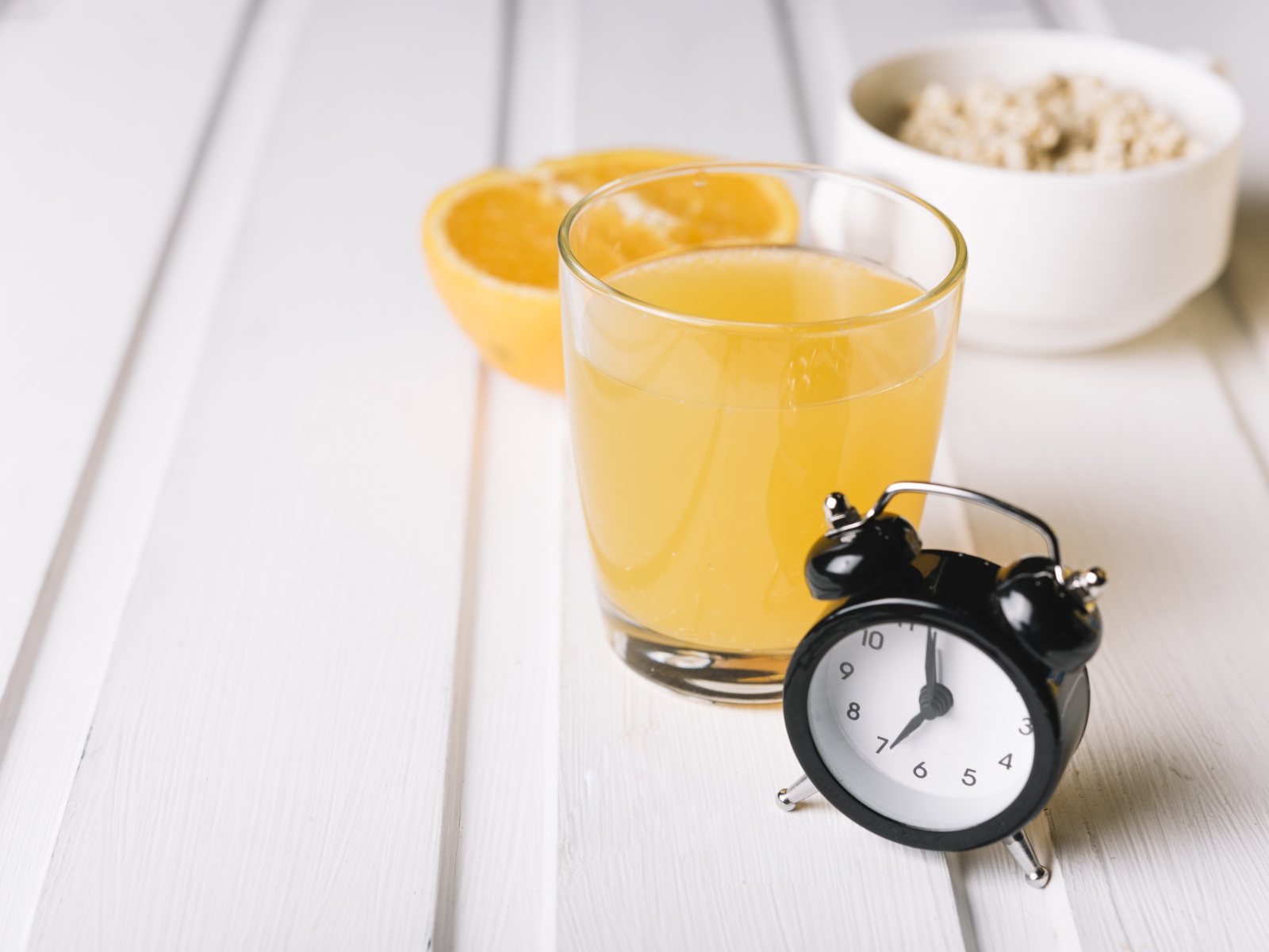 Черный будильник на столе со стаканом сока и хлопьями 