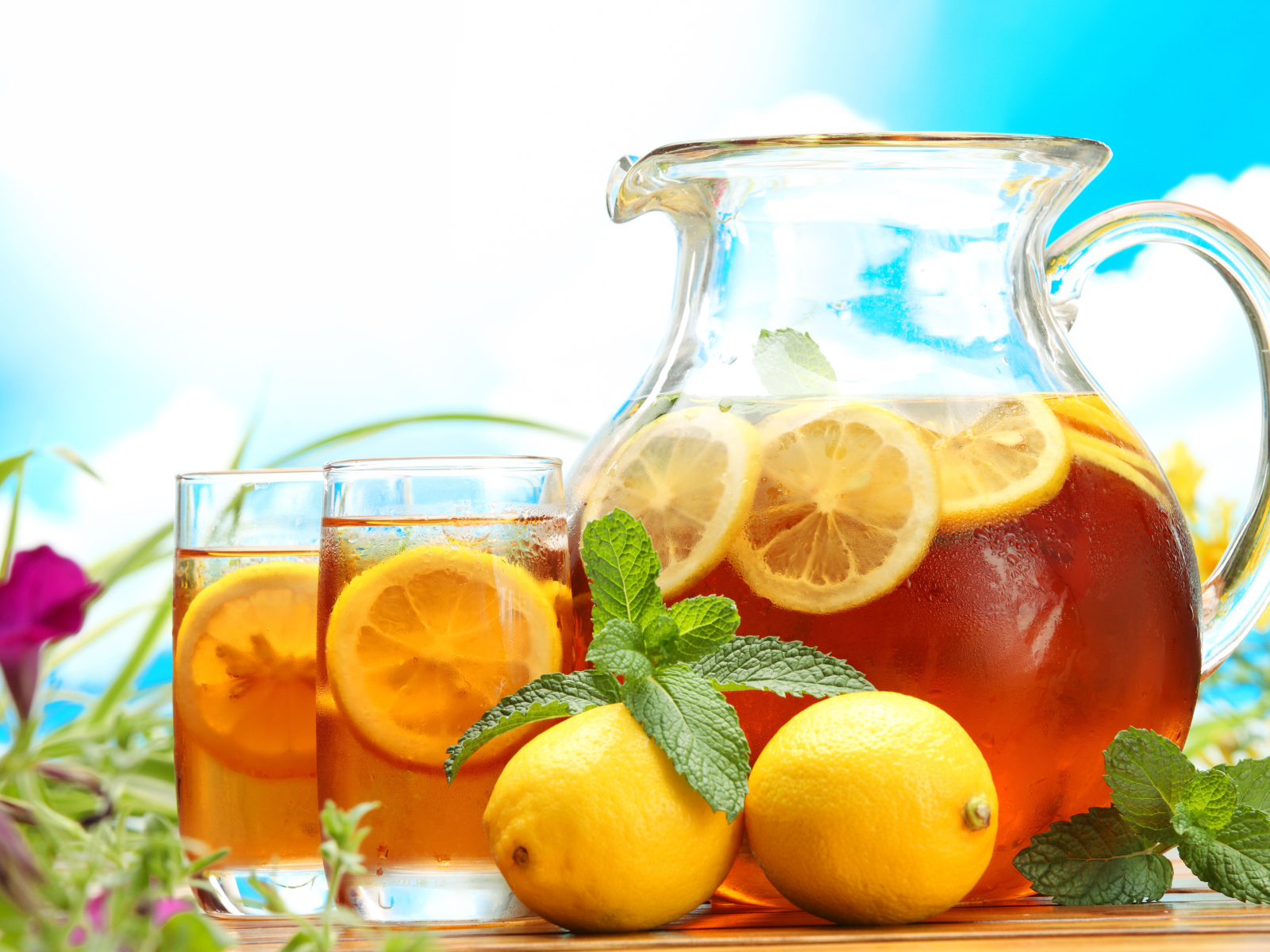 Холодный лимонад в графине на столе со стаканами и плодами лимона